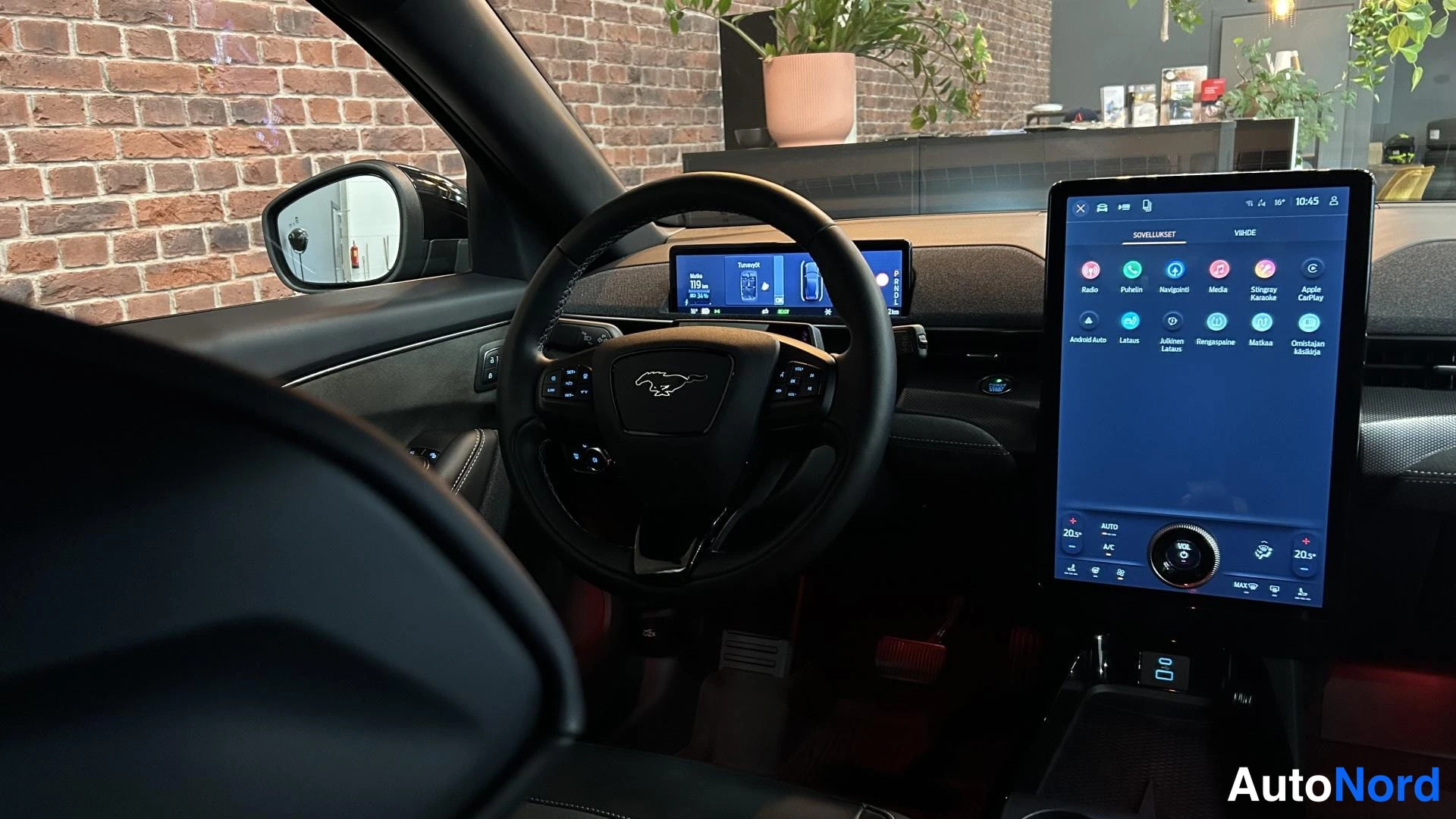 Muu: Ohjaamo sisäapäältä: Ford-ohjauspyörä, pystysuora infotainment-näyttö sovellusvalikolla ja digitaalinen mittaristo, tumma sisusta.