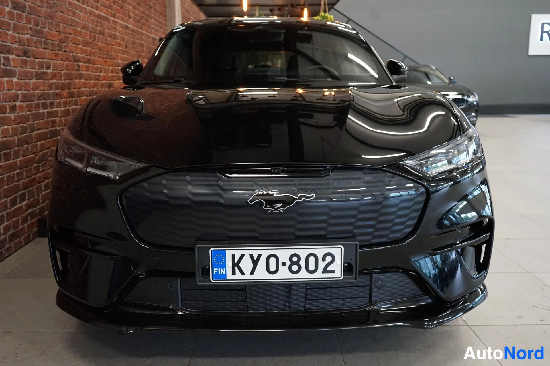 Edestä: Musta Ford Mustang Mach-E, takaa näkyvä auton etupää rekenteella KY0-802