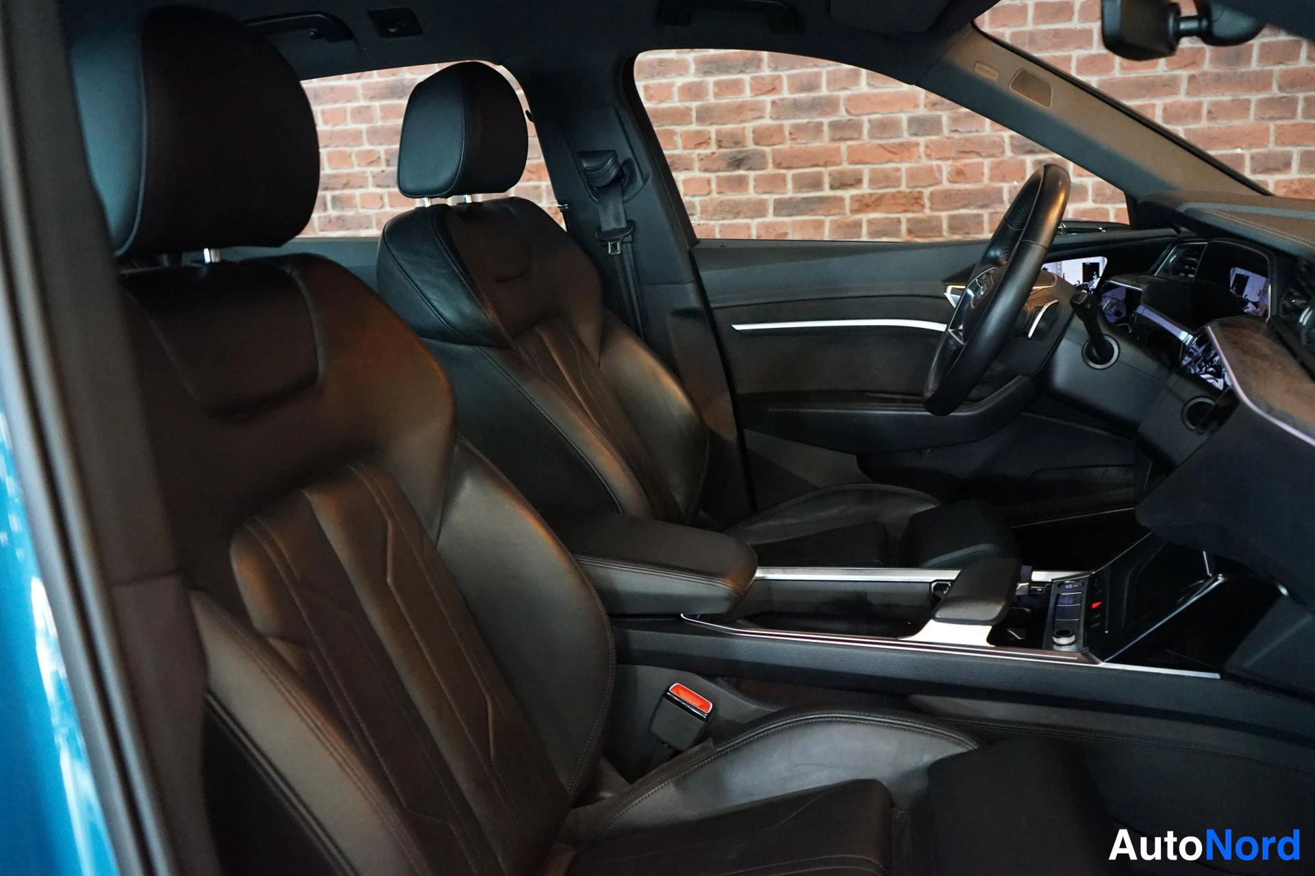 Muu: Audi e-tronin etuosan istuimet ja kojelauta sivulta kuvattuna: mustat sportti-istuimet, ohjauspyörä, kosketusnäyttö ja keskinoka.