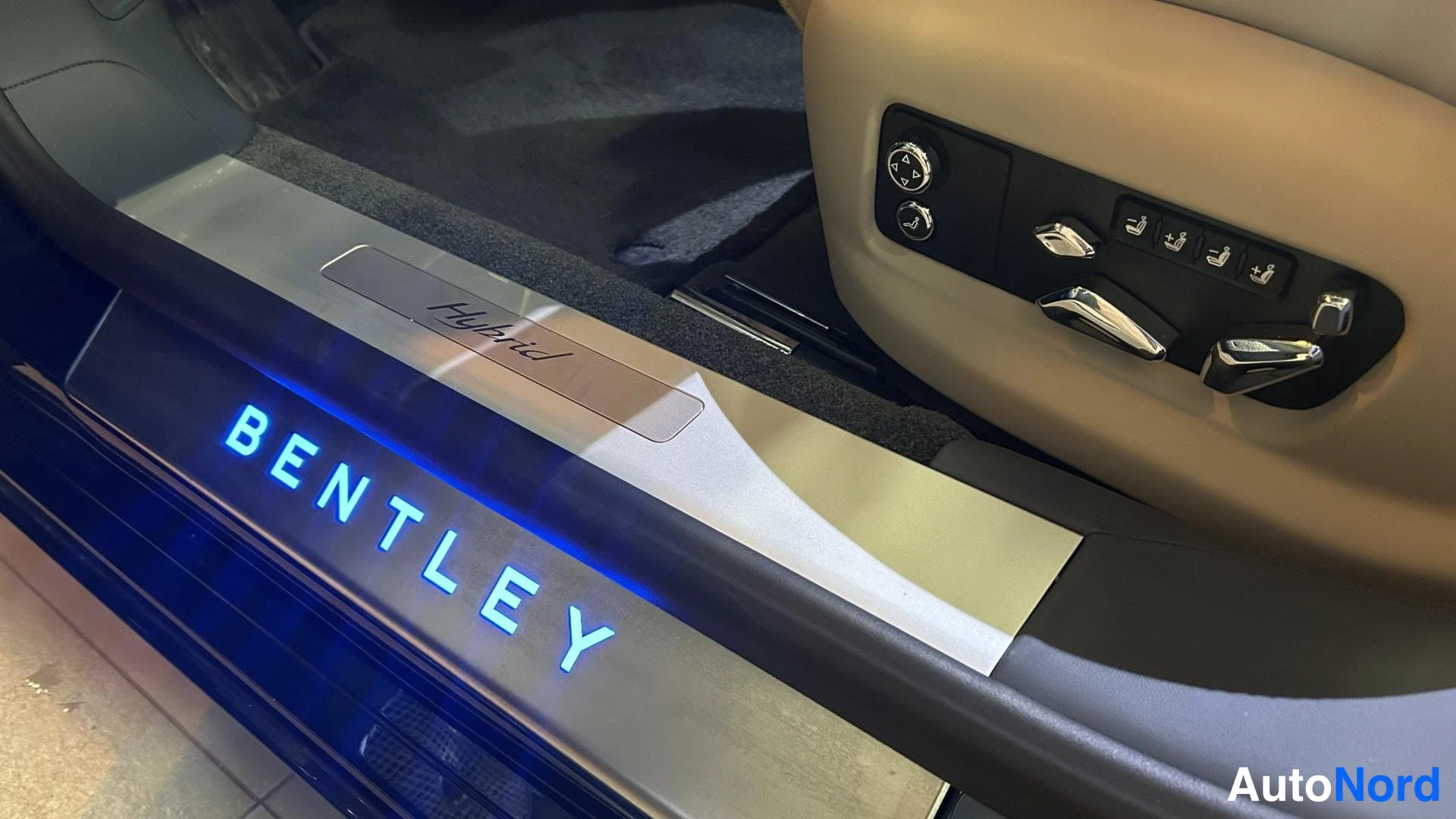 Muu: Oven kynnyslistassa sinisesti valaistu BENTLEY-teksti ja sen yläpuolella metallinen plate jossa lukee Hybrid; istuimen säätöpainikkeita ovipaneelissa.
