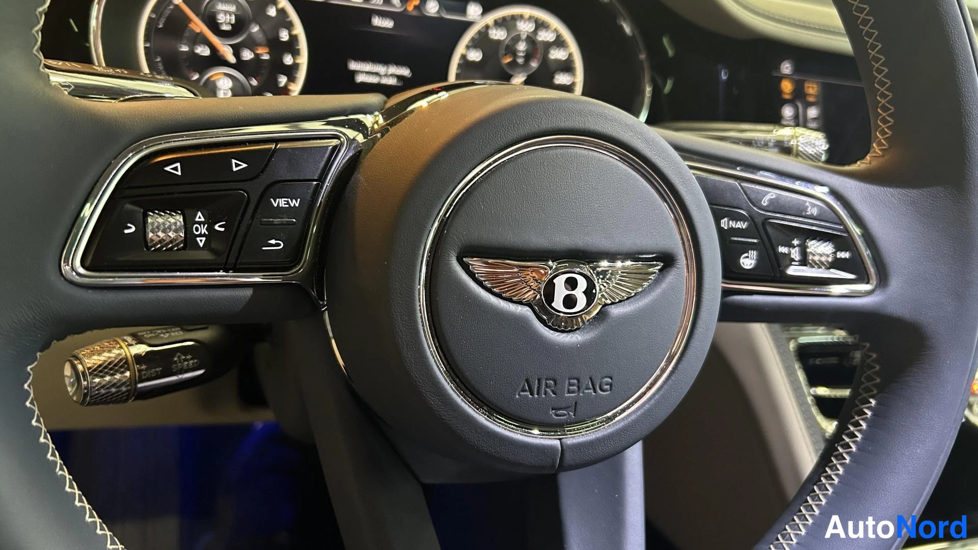 Muu: Bentleyn ohjauspyörän tarkempi kuva: keskussa logo ja AIR BAG -merkintä, vasemmalla pieninäppäimet (VIEW, OK) ja oikealla NAV- ja puhelinpainikkeet.