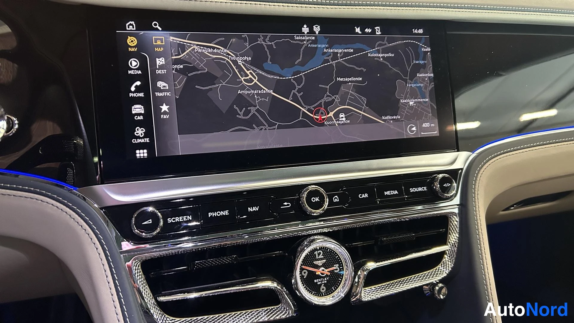 Muu: Keskikonsolin suuri karttana näkyvä kosketusnäyttö navigaattorilla, alla fyysiset painikkeet (SCREEN, PHONE, NAV, OK, CAR, MEDIA, SOURCE) ja Bentley-kello.