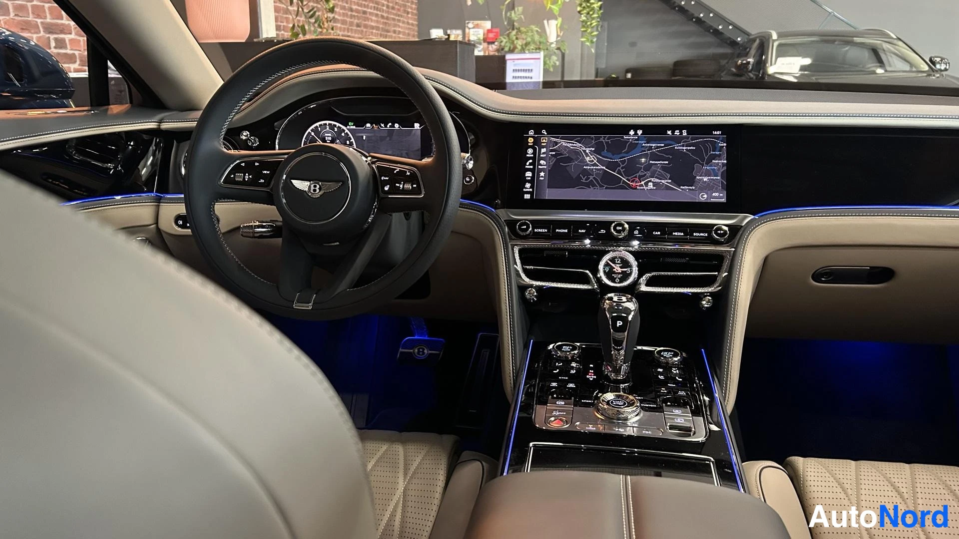Edestä: Kulmanäkymä ohjaamosta: Bentley-ohjauspyörä, karttanäyttö ja keskikonsolin valitsimet.