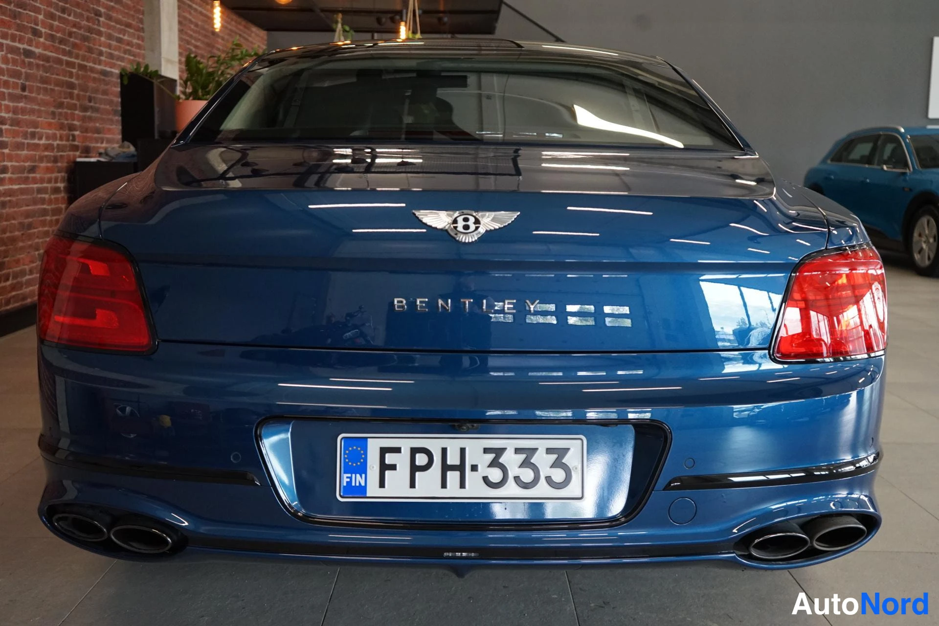 Takaa: Sinisen auton takapää kojiessa, BENTLEY-teksti takaluukussa ja neljä pakoputkea, rekisteritunnus.