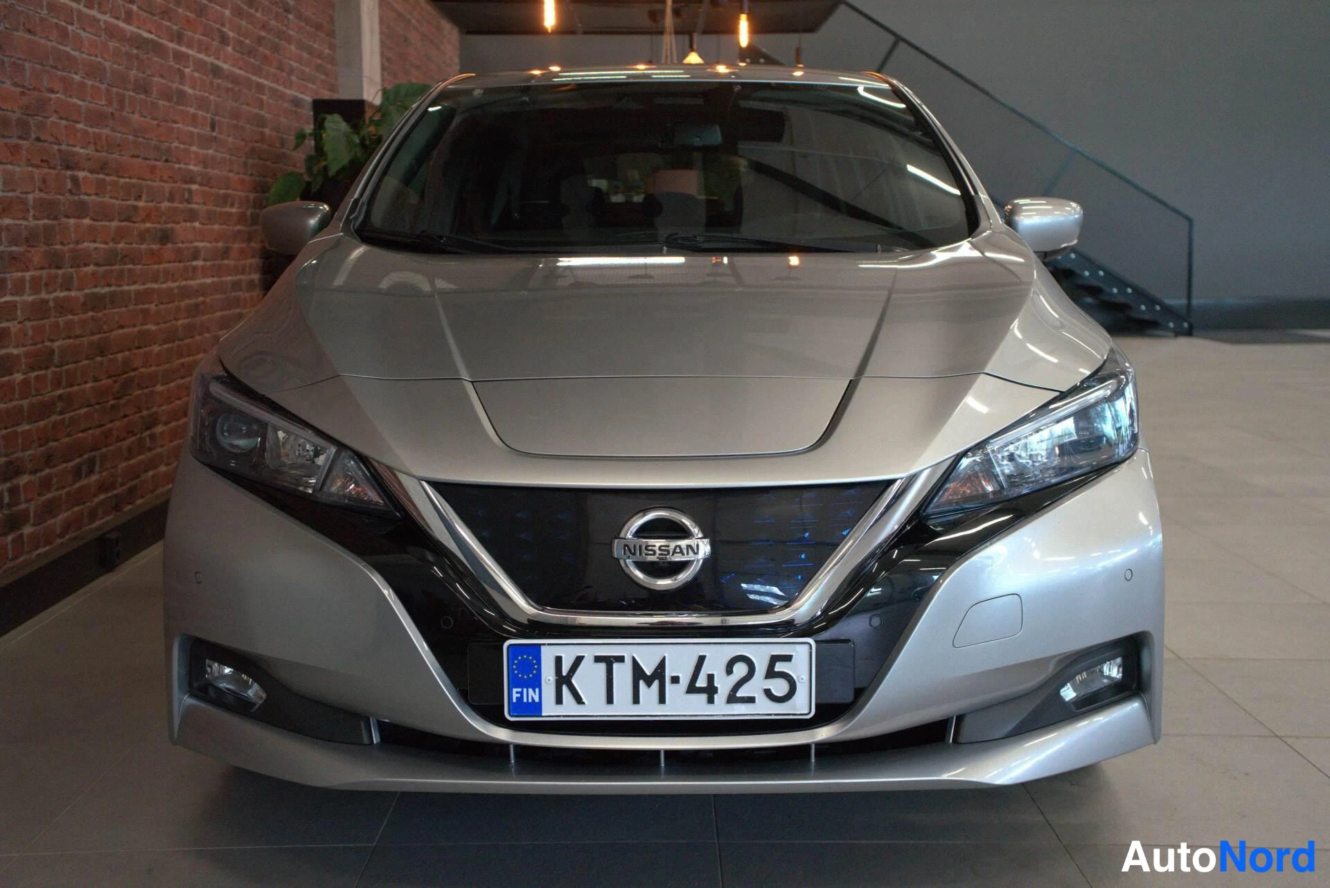 Edestä: Nissan Leafin etupää edestäpäin: hopeansävyinen kori, musta etusäleikkö Nissan-emblemillä, kapeat LED-ajovalot ja SIN-rekisterikilpi.