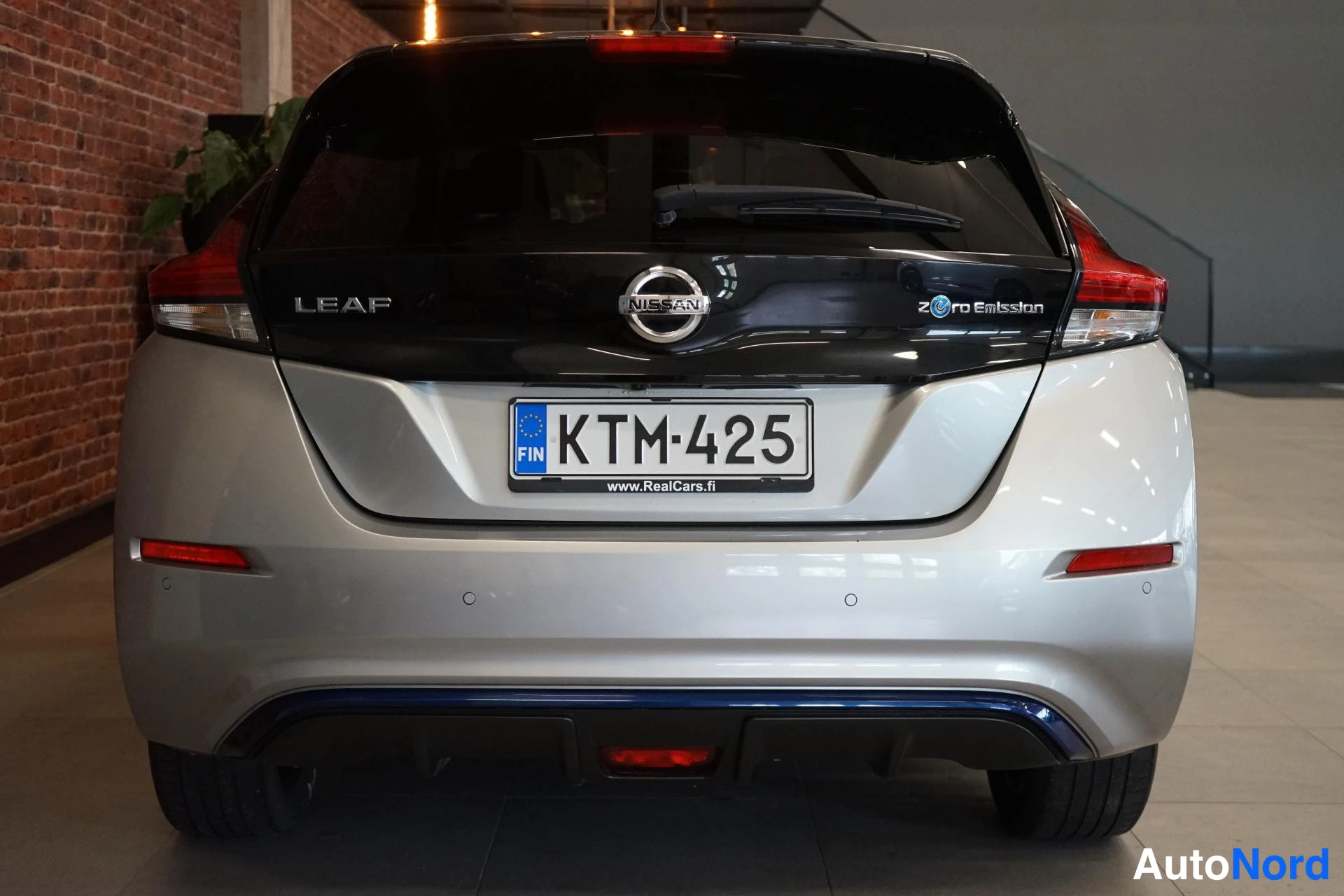 Takaa: Nissan Leafin takaosa suoraan takaa: LEAF-teksti ja Zero Emission -merkintä takaluukun mustalla paneelilla, SIN-rekisterikilpi, punaiset takavalot ja sininen ko