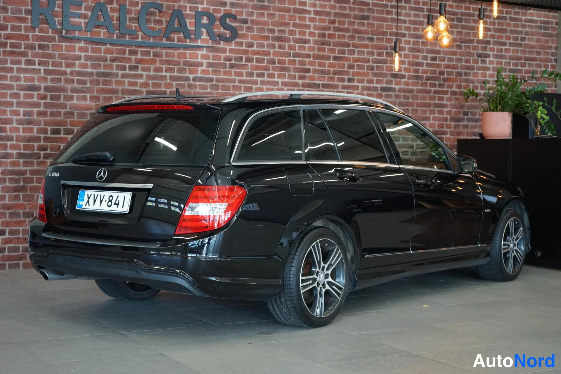 Takaviisto: Musta farmariauto Mercedes-Benz, takaosa ja oikea kylä näkyvissä, rekisteritunnus, kattokaiteet ja hopeavanteet.