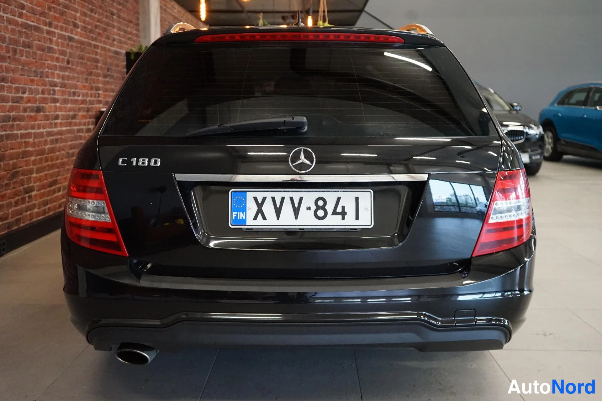 Takaa: Mustan Mercedes-Benzin takapää suoraan takaa: C 180 -merkintä, takaladon logo ja rekisteritunnus.