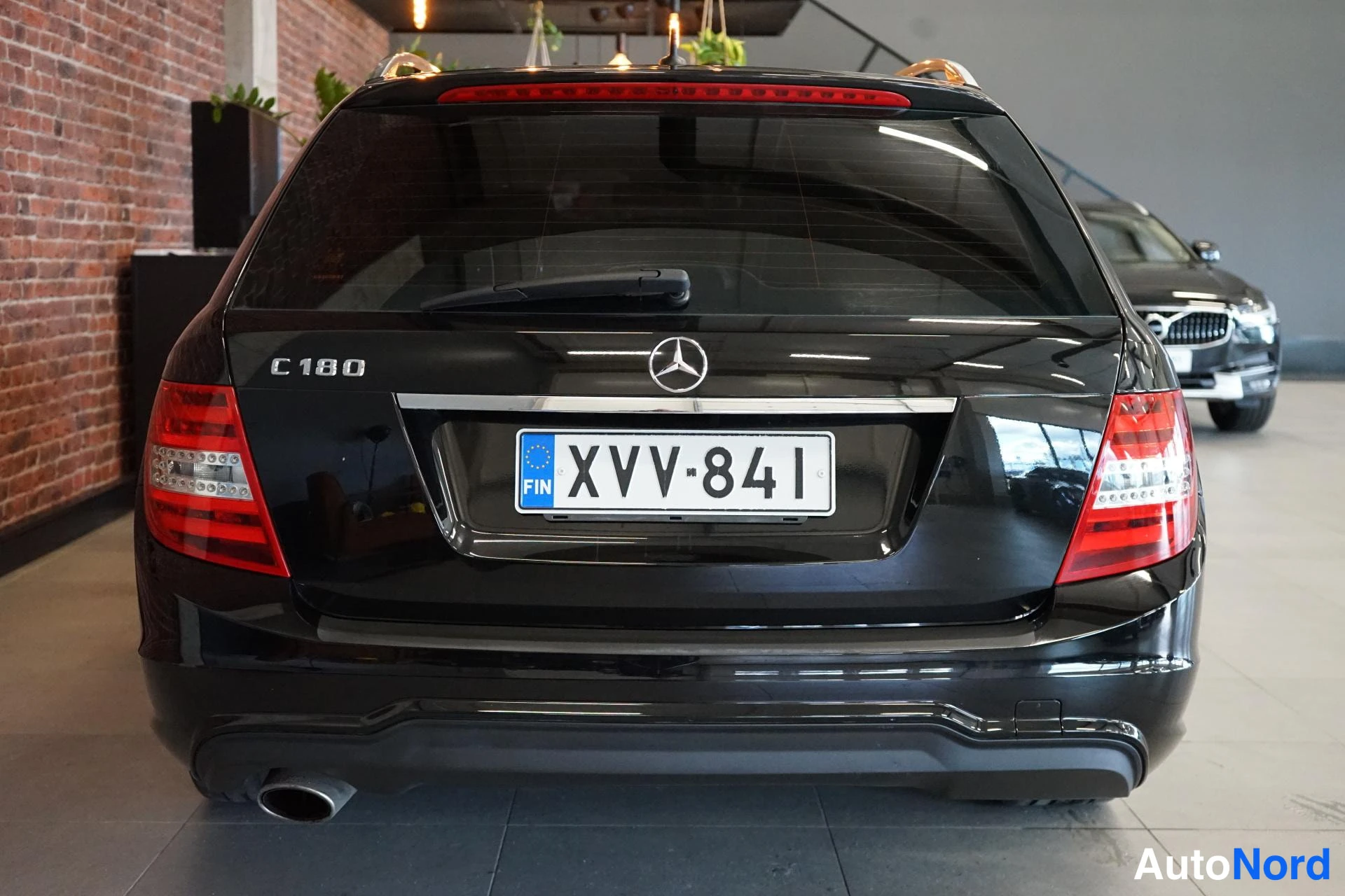 Takaa: Mercedes-Benzin musta takaosa suoraan takaa: C 180 -merkintä, kolmas jarruvalo, takakaistahirskojen viivat ja rekisteritunnus.