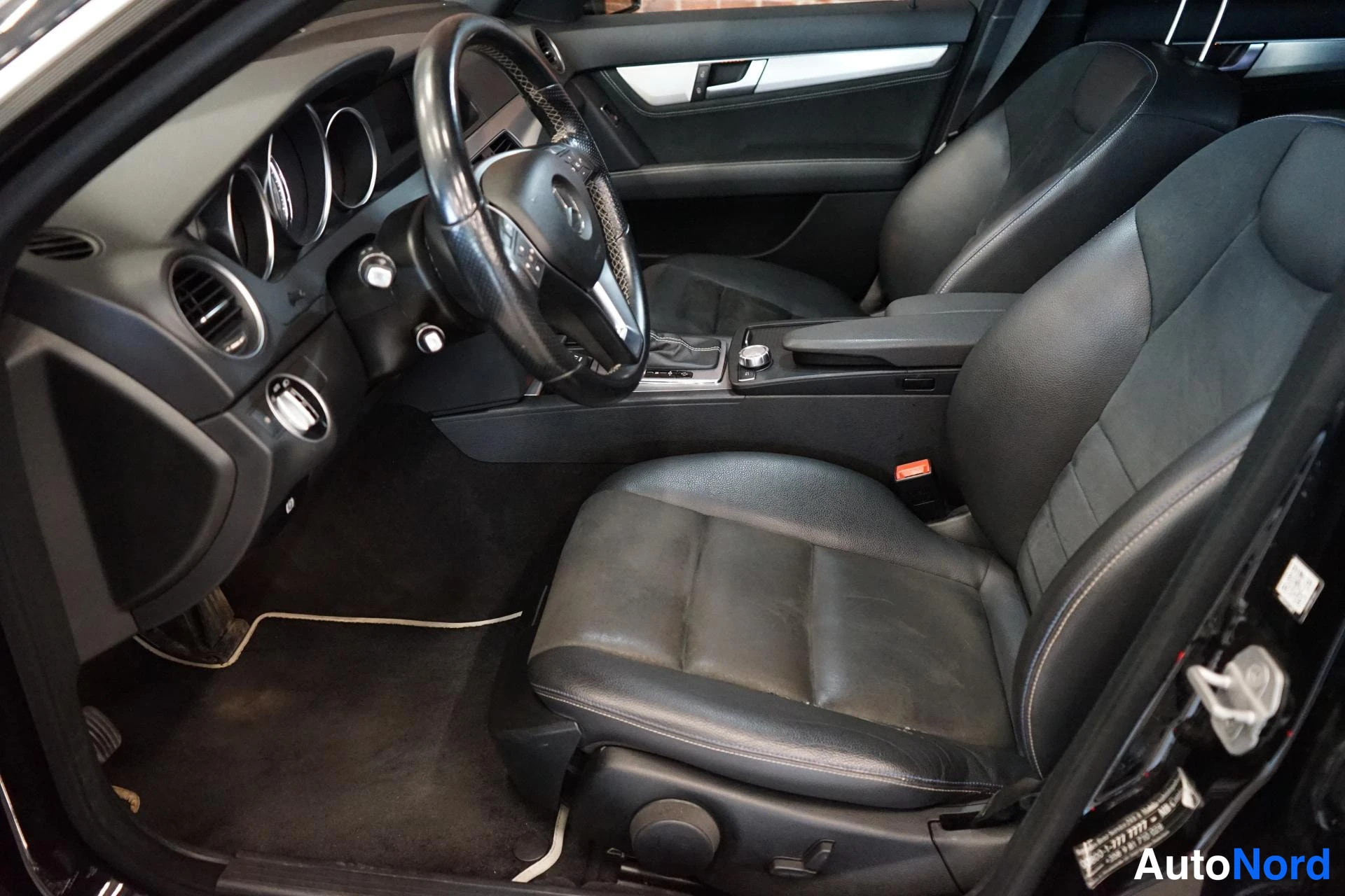 Muu: Mercedes-Benzin etuistuimet ja kojelauta mustaa nahkasisustaa avatusta ovasta katsottuna.