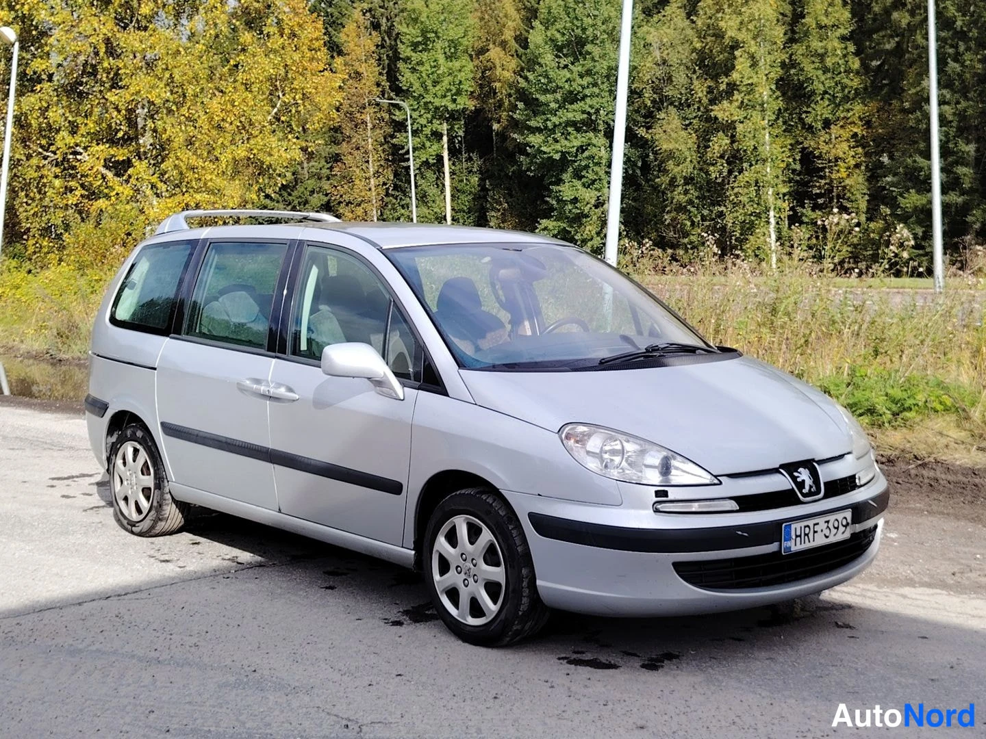 Etuviisto, nokka vasemmalle: Hopeanvärinen tila-auto kuvattu etukolmasosan kuvakulmasta vasemmalle; rekisterikilpi, kattotelineet ja sivupeili.