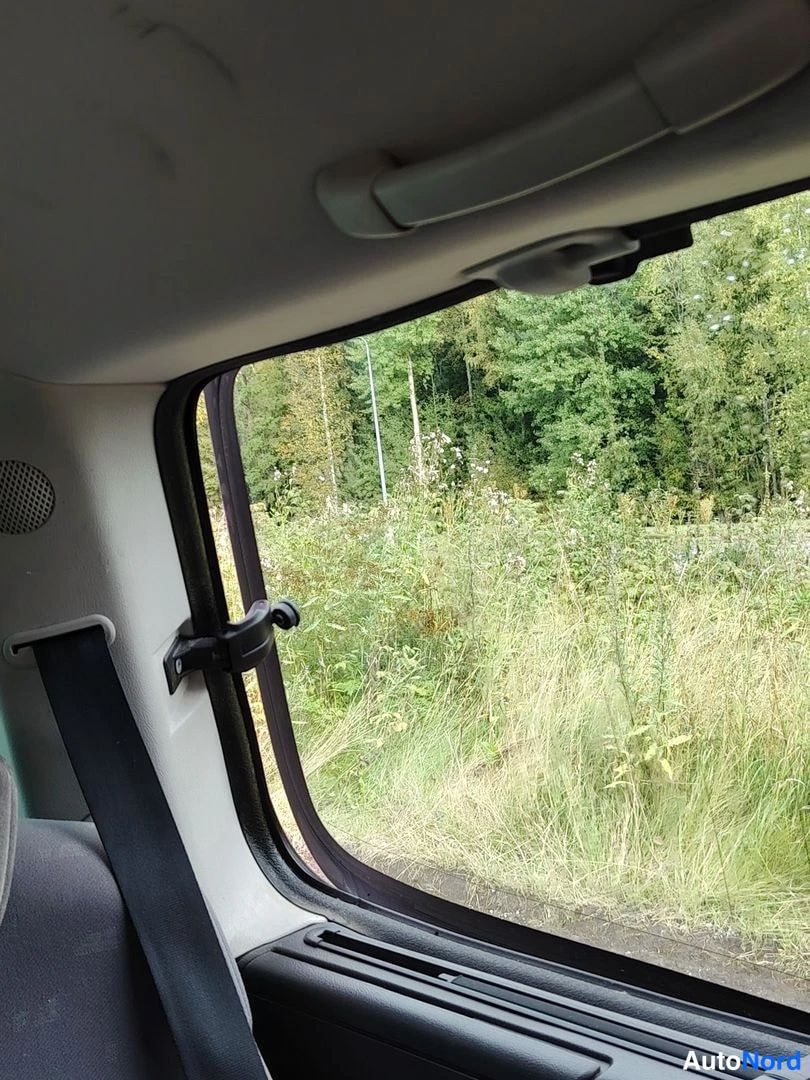 Muu: Sisäovesta ja B-pilarin alue takaa nähtynä: turvavyön hihnapantta ovella, selkänoja jää osin kuvan ulkopuolelle, ikkunan takana niittyä ja metsää.