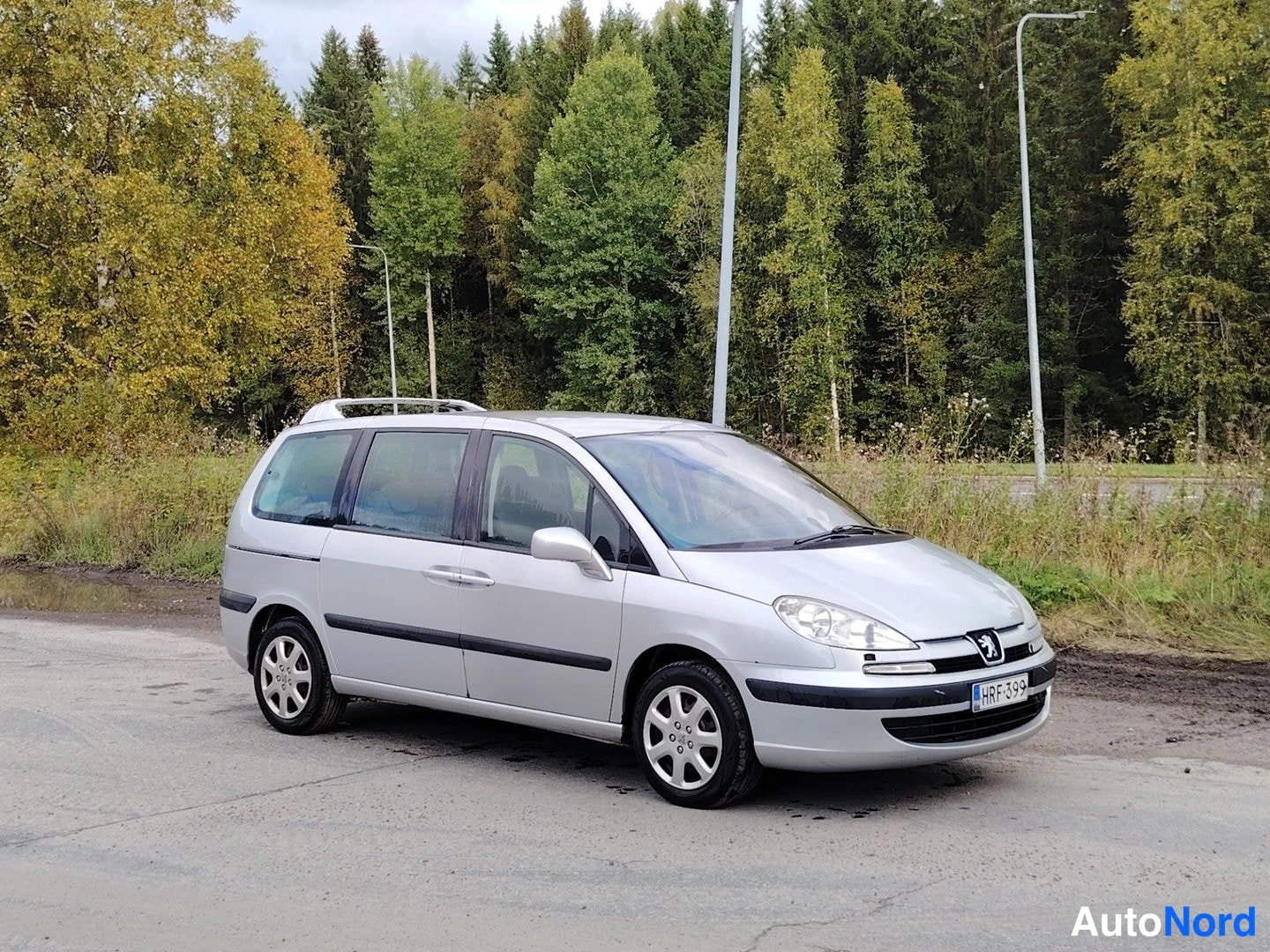 Etuviisto, nokka vasemmalle: Hopeanvärinen tila-auto etukolmisella kuvakulmalla vasemmalta; rekisterikilpi, kattotelineet ja hopeanvärinen kori.