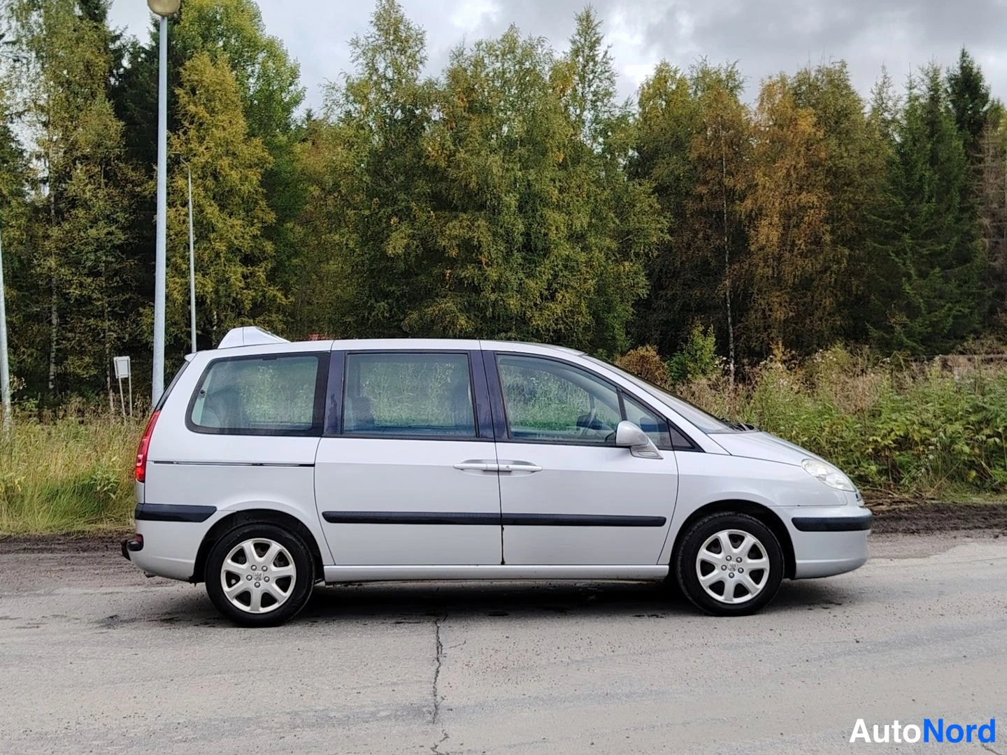 Etuviisto, nokka oikealle: Hopeanvärinen tila-auto sivulta etukulmasta, keula oikealla, kattoine ja pyörineen.