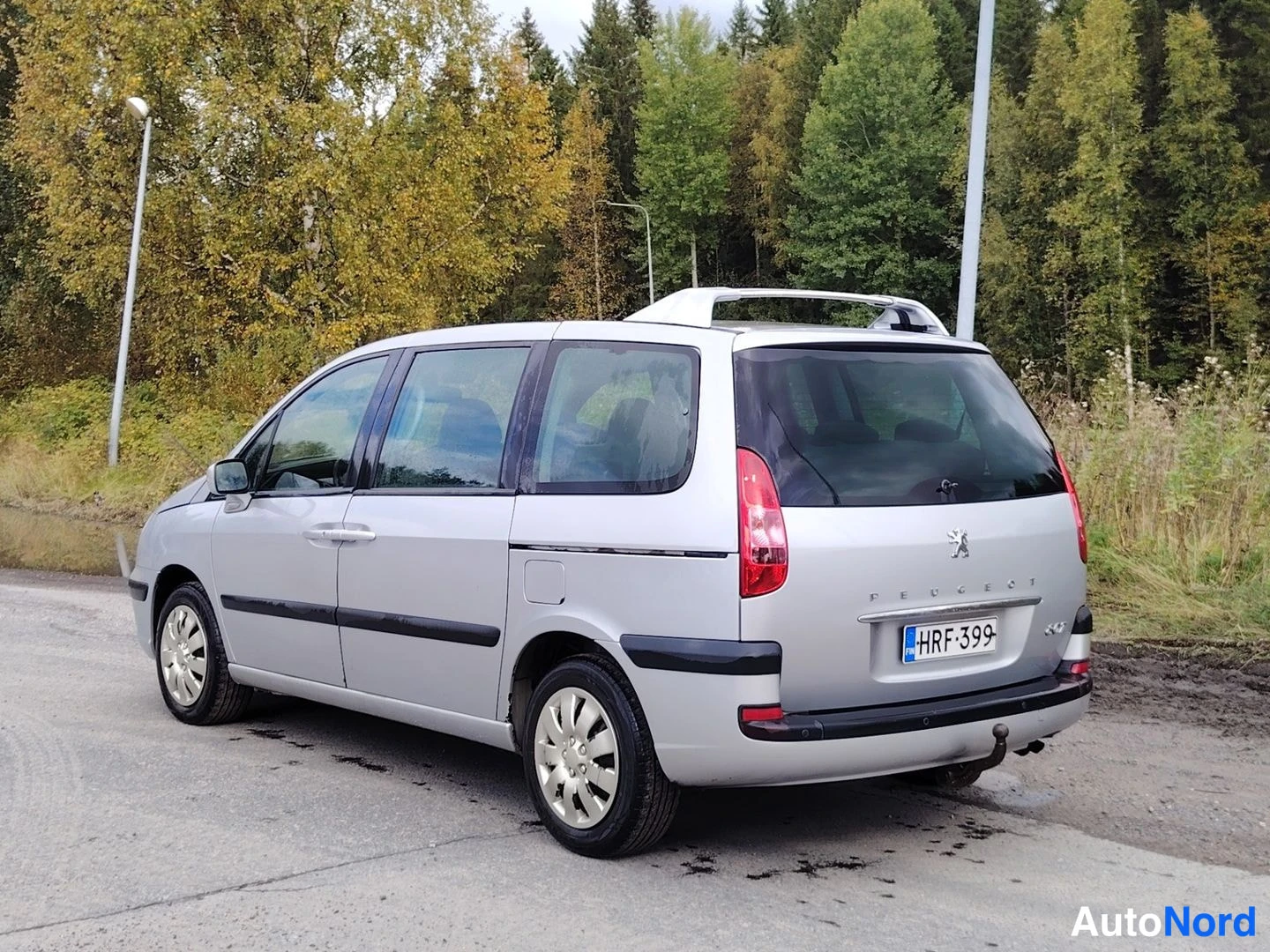 Takaviisto: Hopeanvärinen tila-auto takakulmasta vasemmalta, takavalot ja rekisterikilpi näkyvissä.