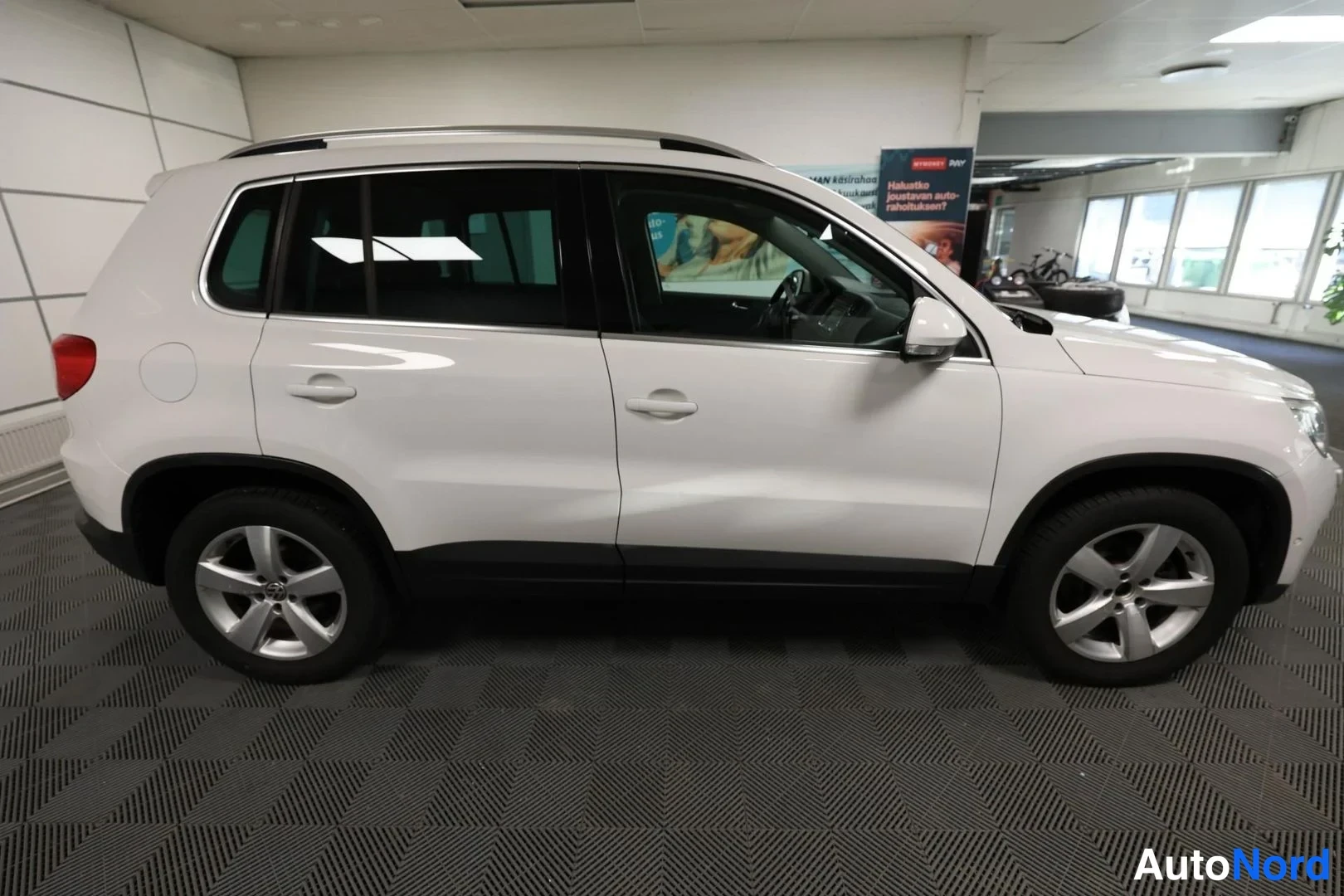 Sivulta: Valkoinen Volkswagen Tiguan -maasturin sivunäkymä sisätiloissa, kylki ja molemmat pyyät näkyvissä.