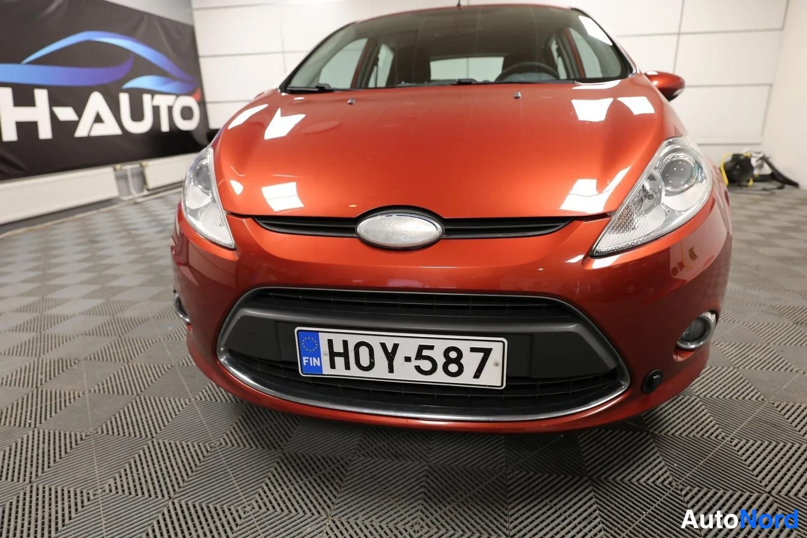Edestä: Auton etusta suoraan: tummansininen kyltti etupuskurin mustassa upotuksessa; ajovalot ja Ford-merkki näkyvät.