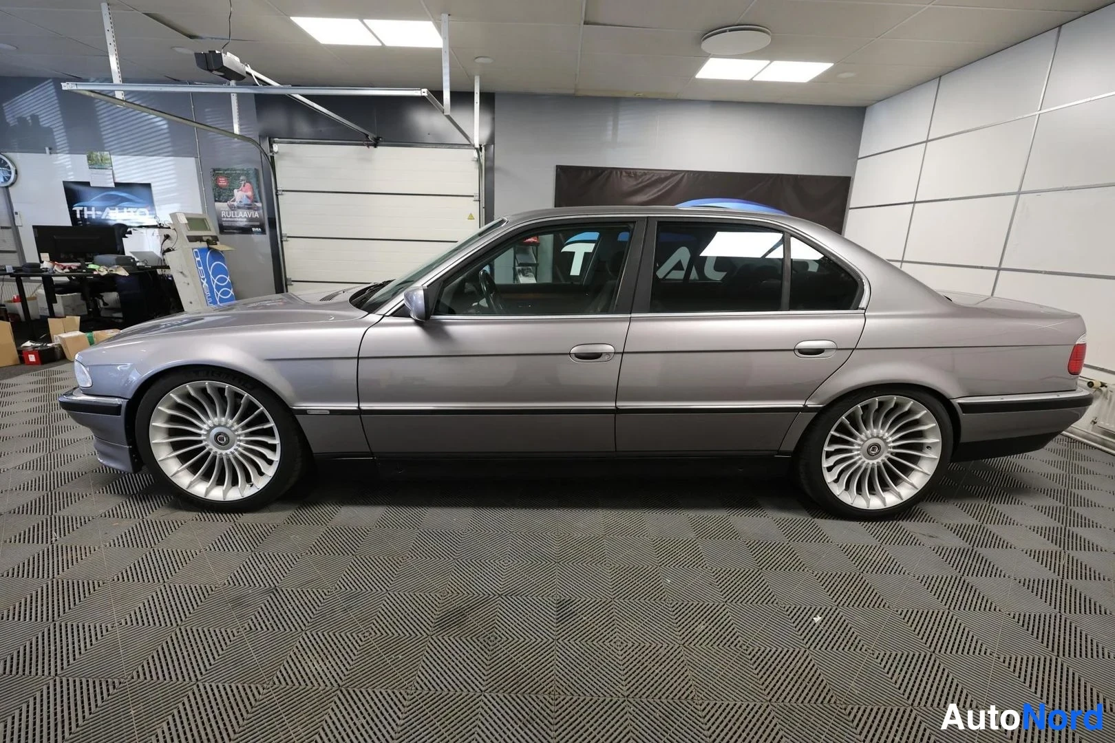 Sivulta: BMW-sedan sivuprofiili oikealta vasemmalle autotallissa, hopeanharmaa kori