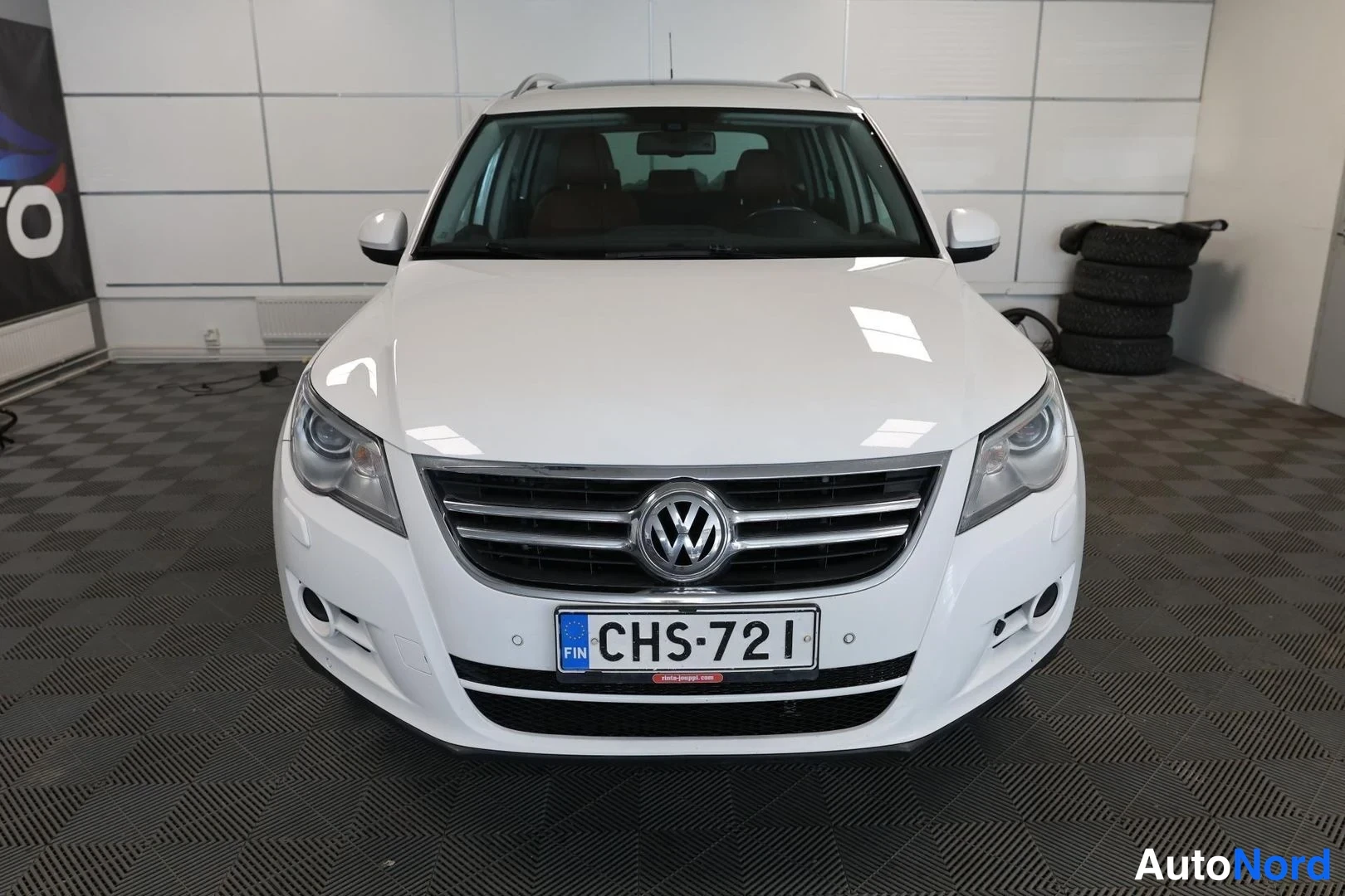 Edestä: Valkoisen Volkswagen Tiguamin etunäkymä, VW-merkki säleikkössä ja rekisterikilpi.