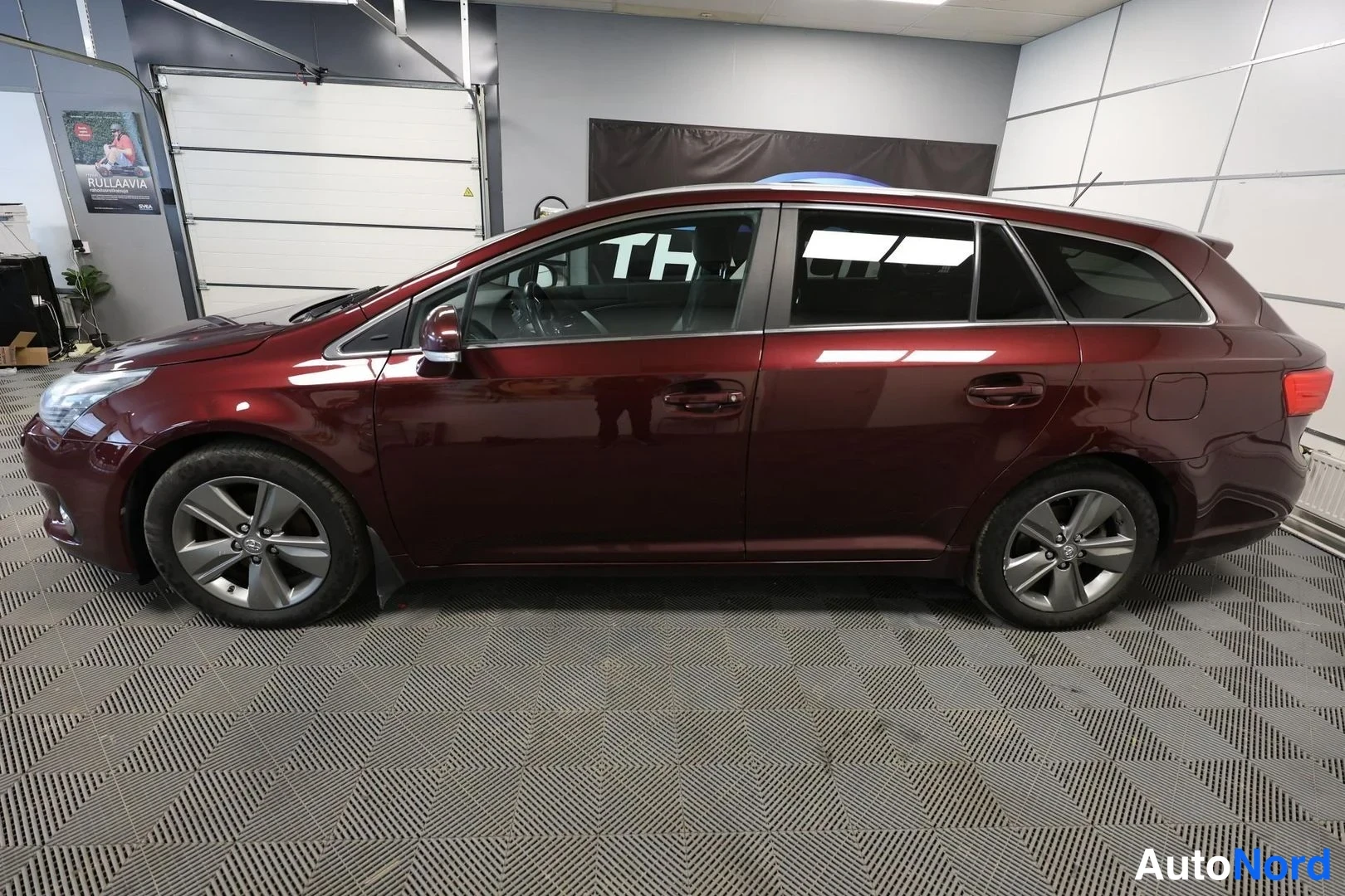 Sivulta: Tummansinisen Toyota Avensis -farmarin sivuprofiili sisätiloissa, molemmat kyljet näkyvissä