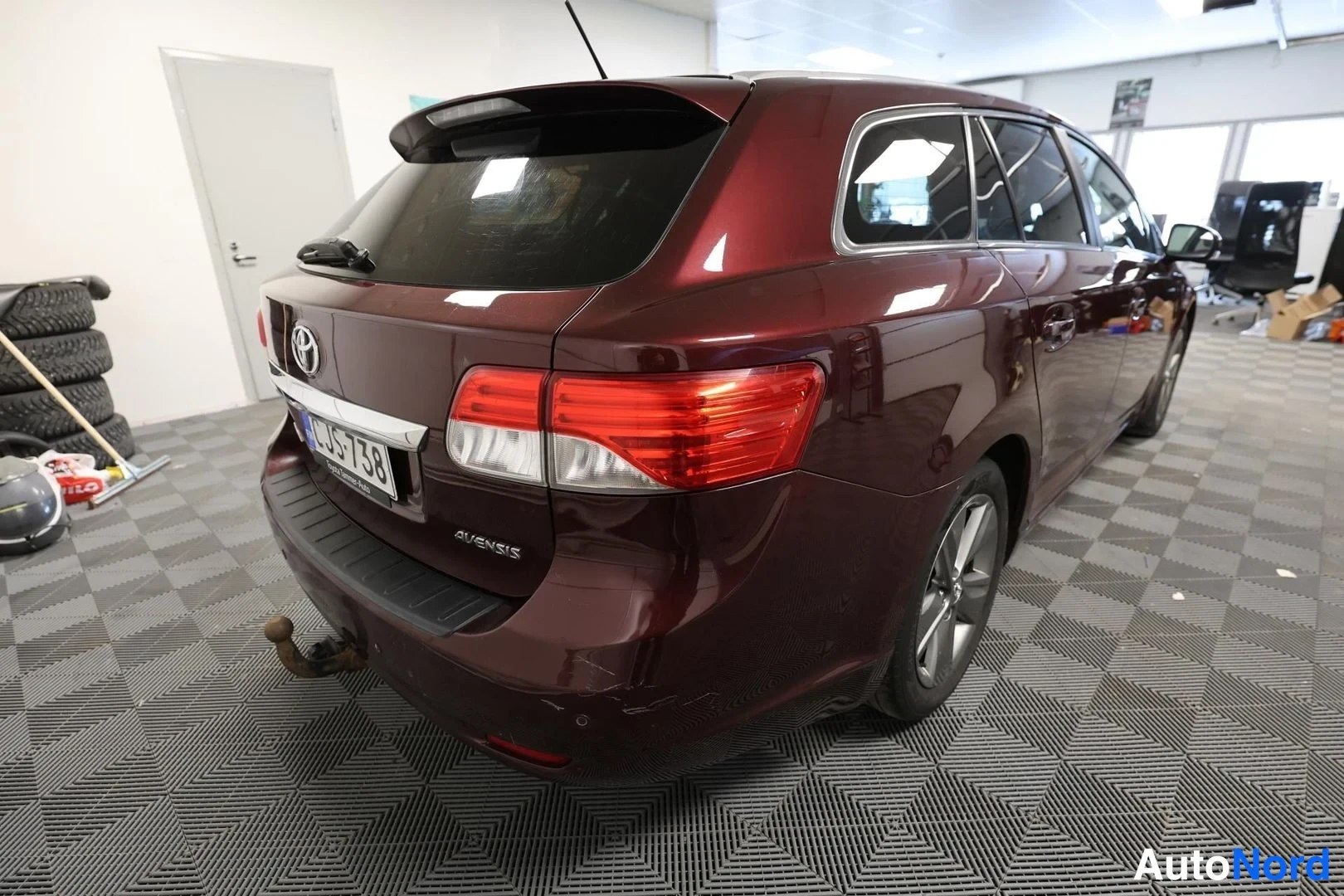 Takaviisto: Tummansinisen Toyota Avensis -farmarin takapää vasemmalta viistosti, rekisterikilpi ja perävaunukoukku