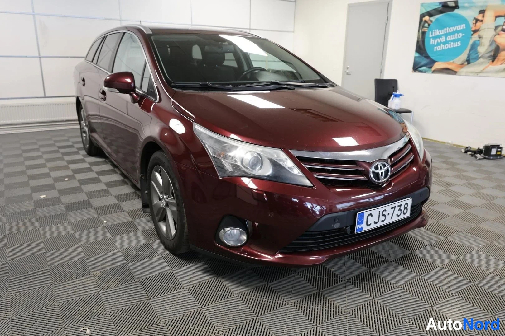 Etuviisto, nokka oikealle: Tummanpunaisen farmariauton etukulma, Toyota-merkki keulaossa ja rekisterikilpi.