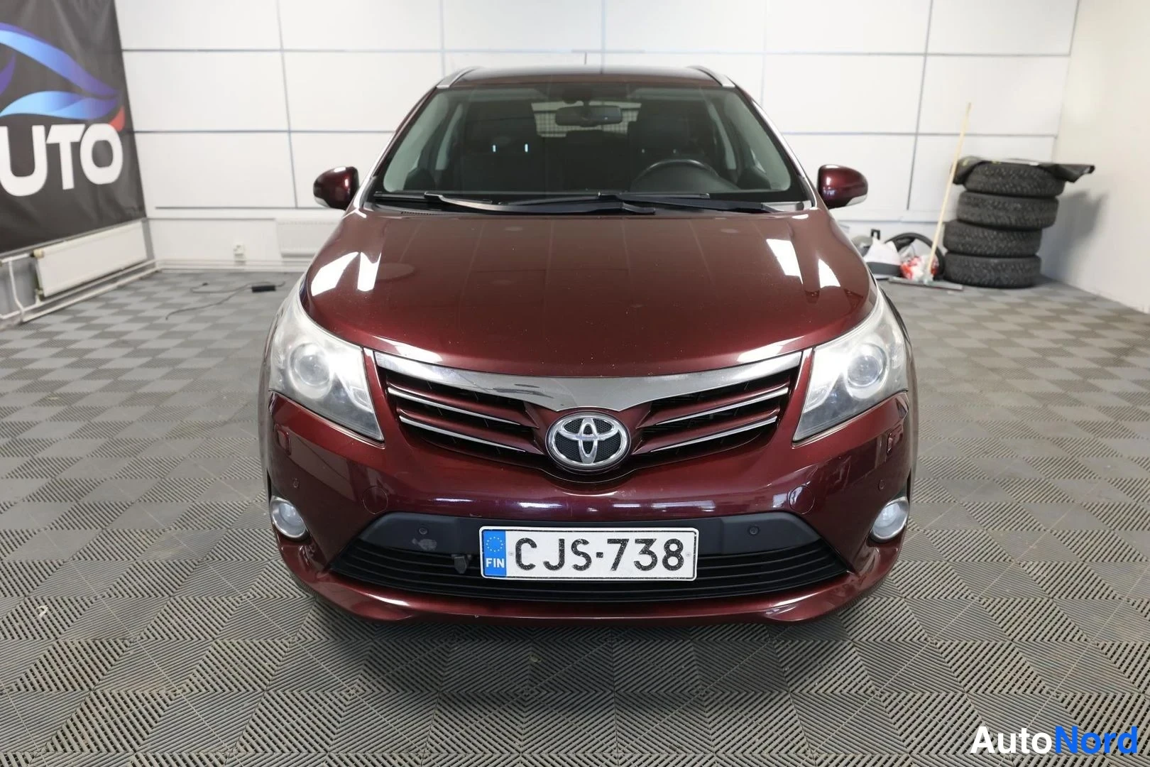 Edestä: Tummanpunaisen farmariauton suora etunäkymä, Toyota-merkki ja rekisterikilpi.