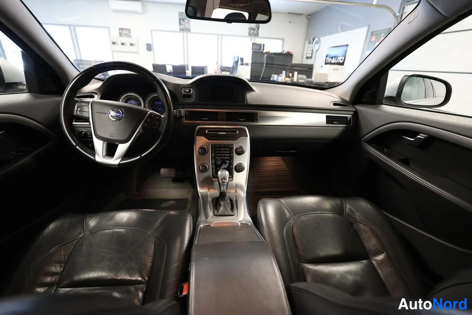 Yksityiskohta: Sisäkuva Volvo V70:stä: ohjauspyörä, kojelauta ja automaattivaihteen valitsin, tummat istuimet.