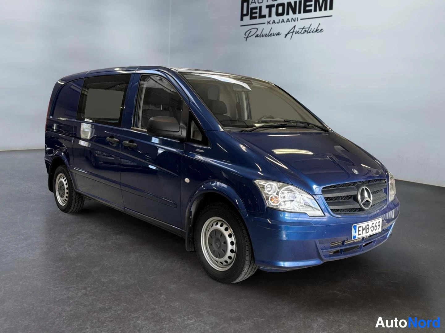 Etuviisto, nokka oikealle: Kolmen neljäsosan etukuva tummansinisestä pakettiautosta, keulakunta ja konepellin Mercedes-tähti näkyvät, rekisteritunnus.