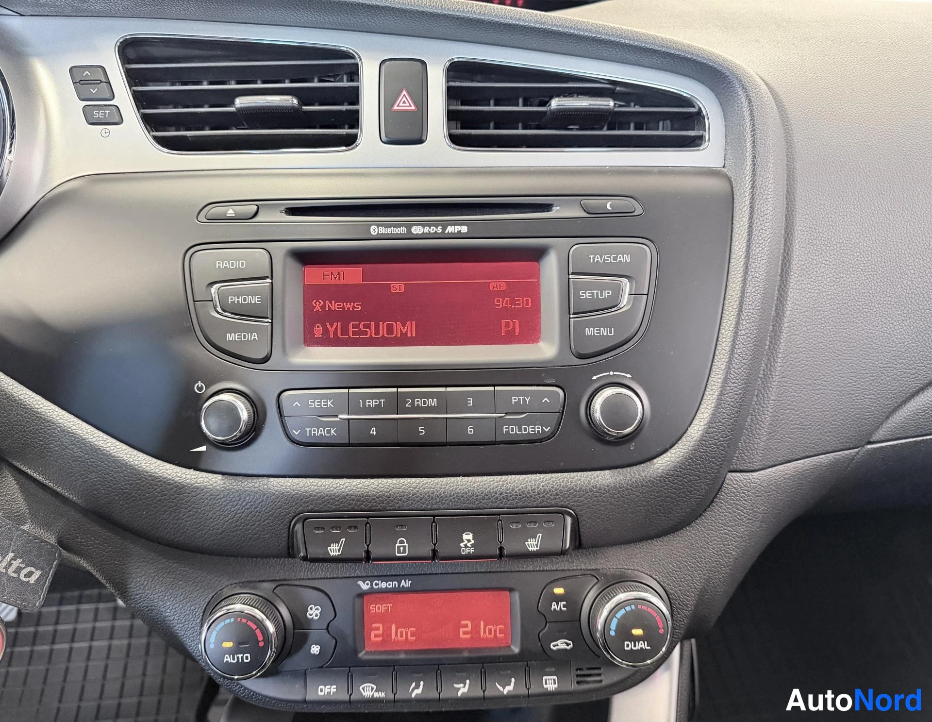 Muu: Lähikuva kojelaudan keskiosasta: radiolaite näytöllä (FM1, News 94,30, YLEISUOMI P1),painikkeet RADIO, PHONE, MEDIA, SETUP, MENU, TA/SCAN; alapuolella istuinläm