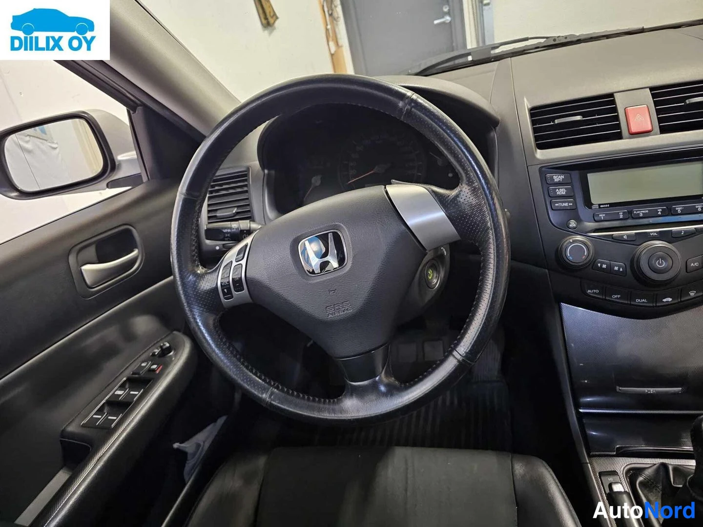 Etuistuimet: Close-up of the driver's perspective showing a three-spoke steering wheel wrapped in worn black leather, silver paddle shifters on the back, and a dual-zone air