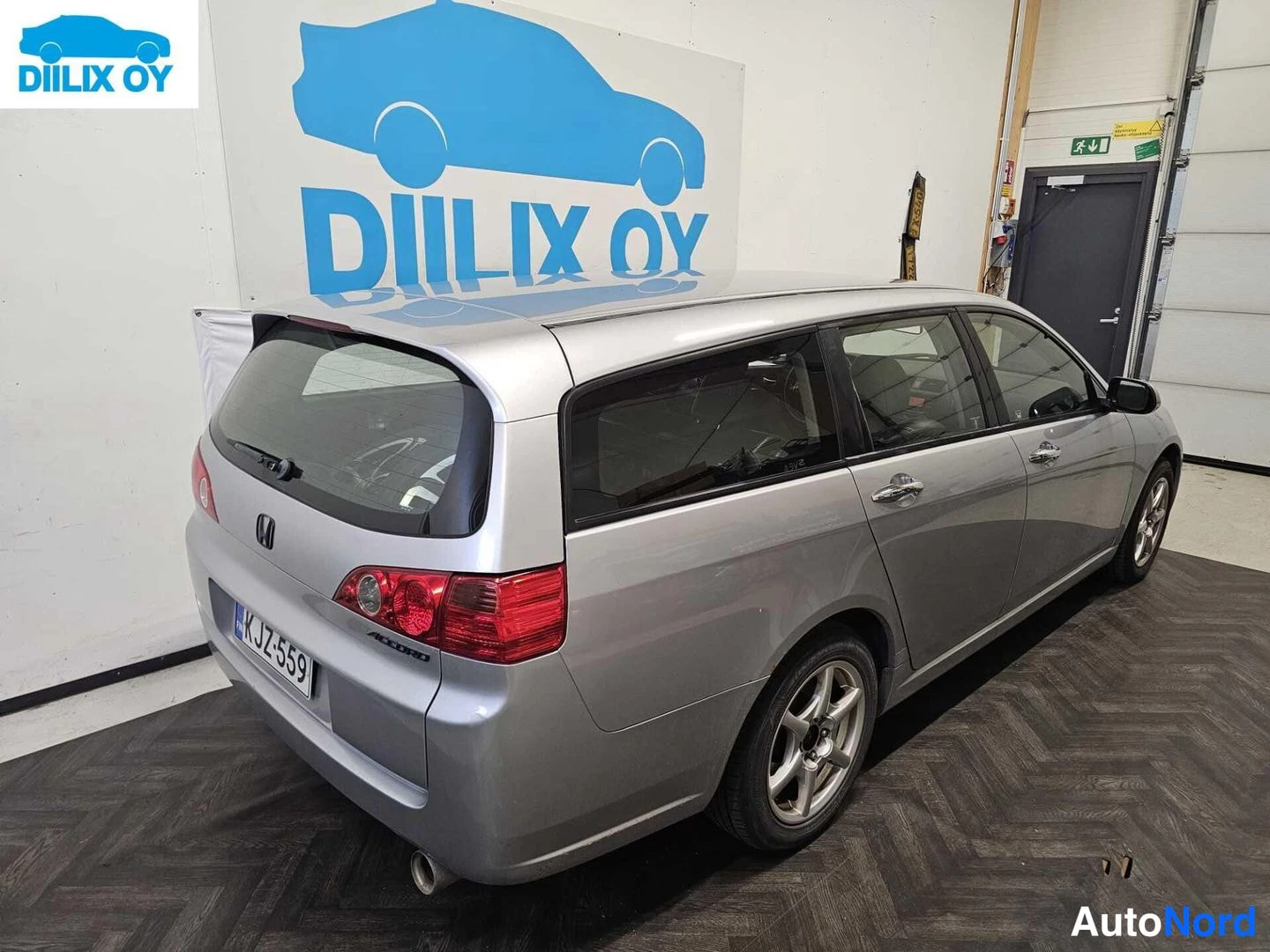 Takaviisto: Silver Honda Accord station wagon photographed from a rear three-quarter angle. The boot lid, tail lights, rear bumper and right flank are clearly visible. A Fi