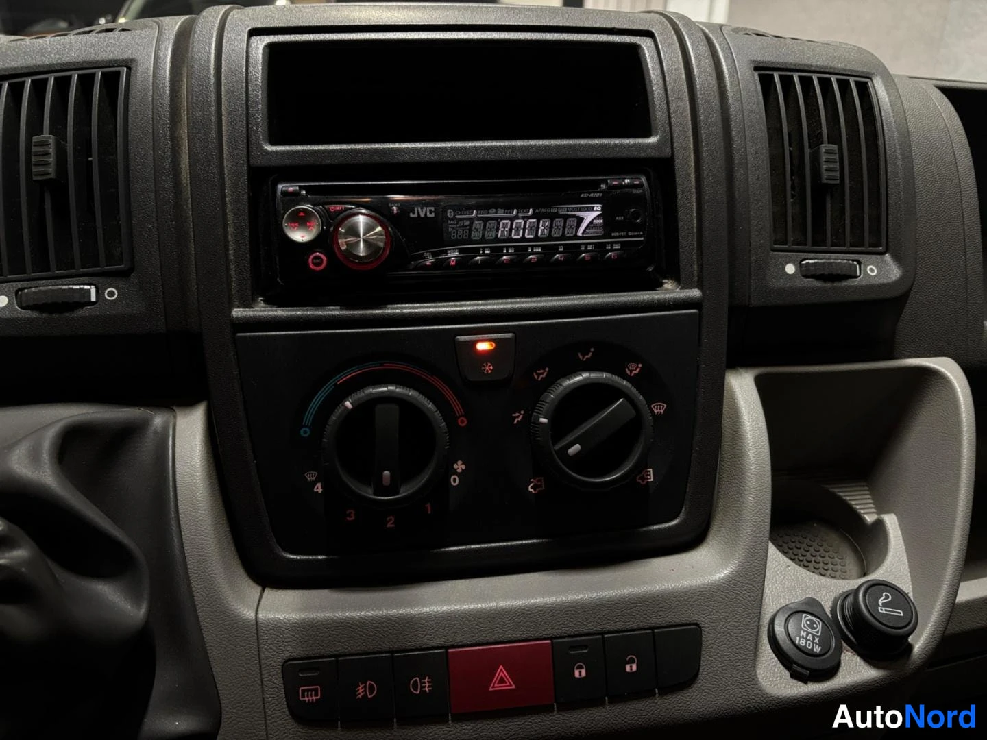 Muu: Lähikuva kojelaudasta: JVC-autoradio, lämmitystöpseli ja 12V-pistoke ja sytytinsäädin.