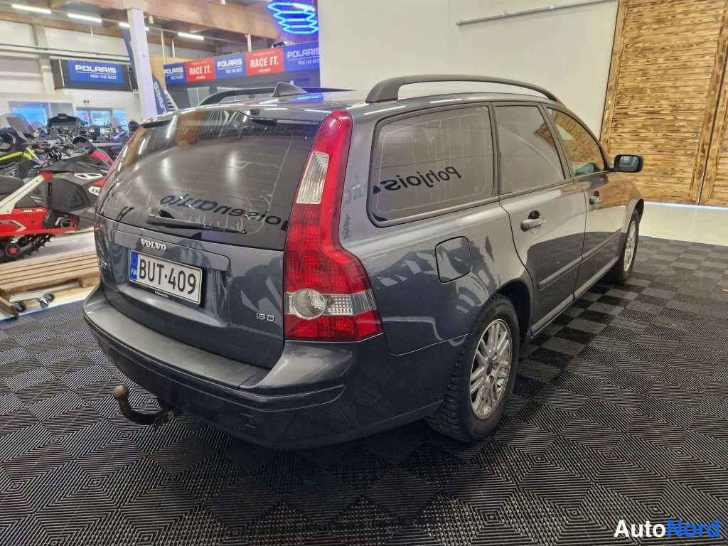 Takaviisto: Harmaa farmariauto kuvattu takaviistöstä sisätiloissa, takapuoli ja oikea sivu näkyvissä, rekisterikilpi.