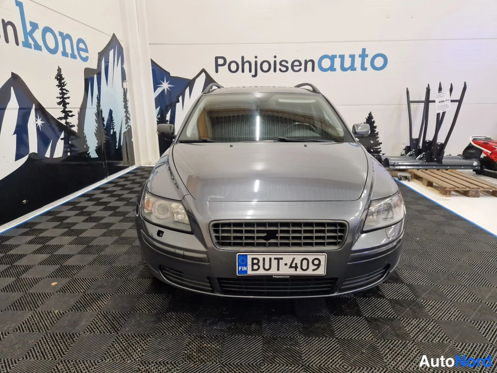 Edestä: Suora kuva auton keulasta, harmaassa farmariautossa suomalainen rekisterikilpi.