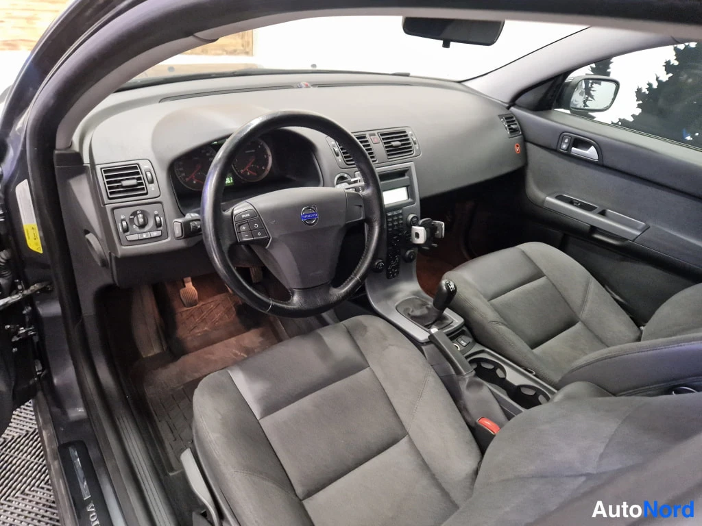 Muu: Auton ohjaamo: Volvo-merkkinen ohjauspyörä, kojelauta ja tummat penkit, vaihtajanuppi keskikonsolissa.