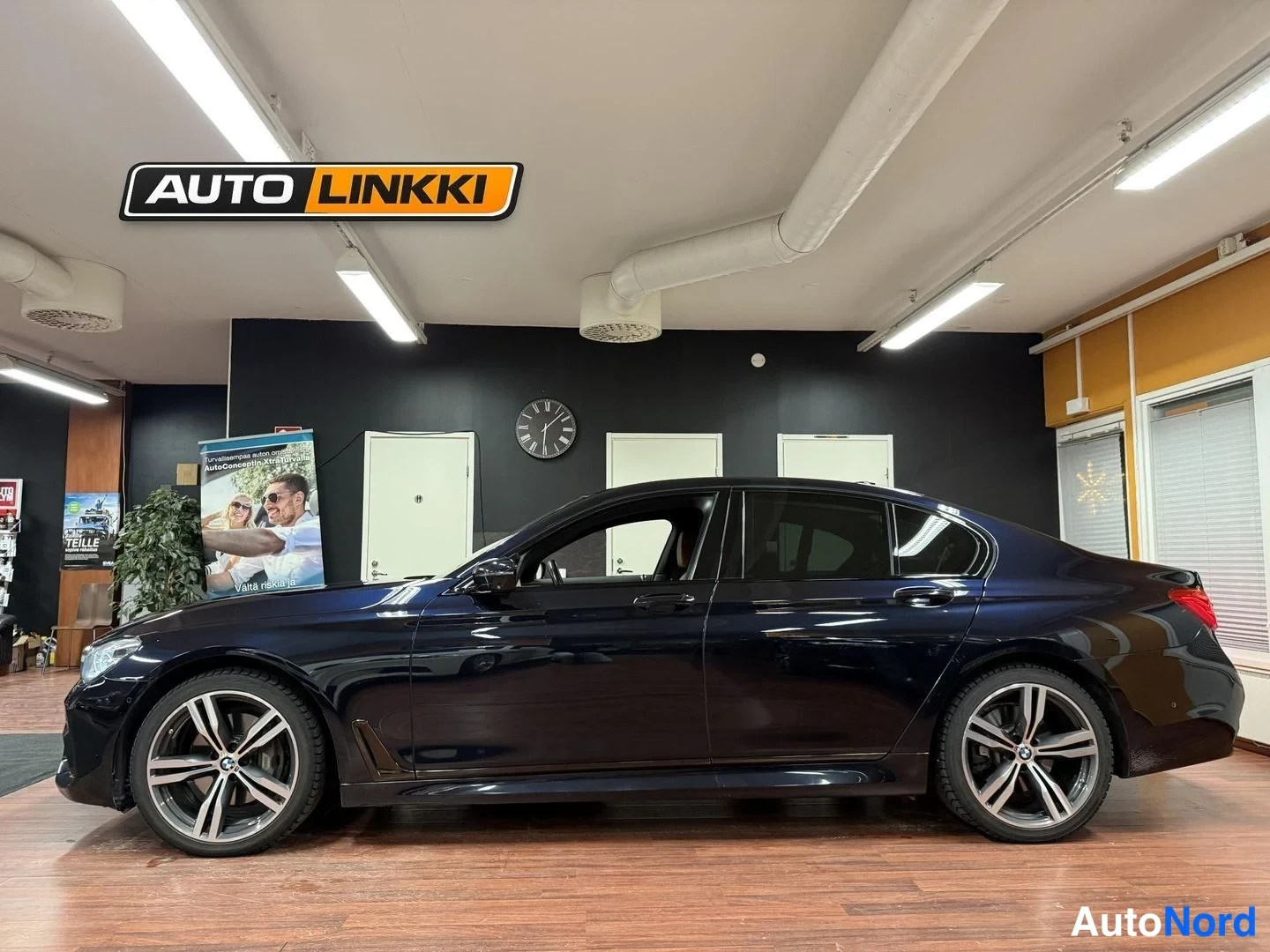 Etuviisto, nokka vasemmalle: Mustan BMW-sedanin sivuprofiili showroomissa, keulakilpi ja pyörät näkyvissä.