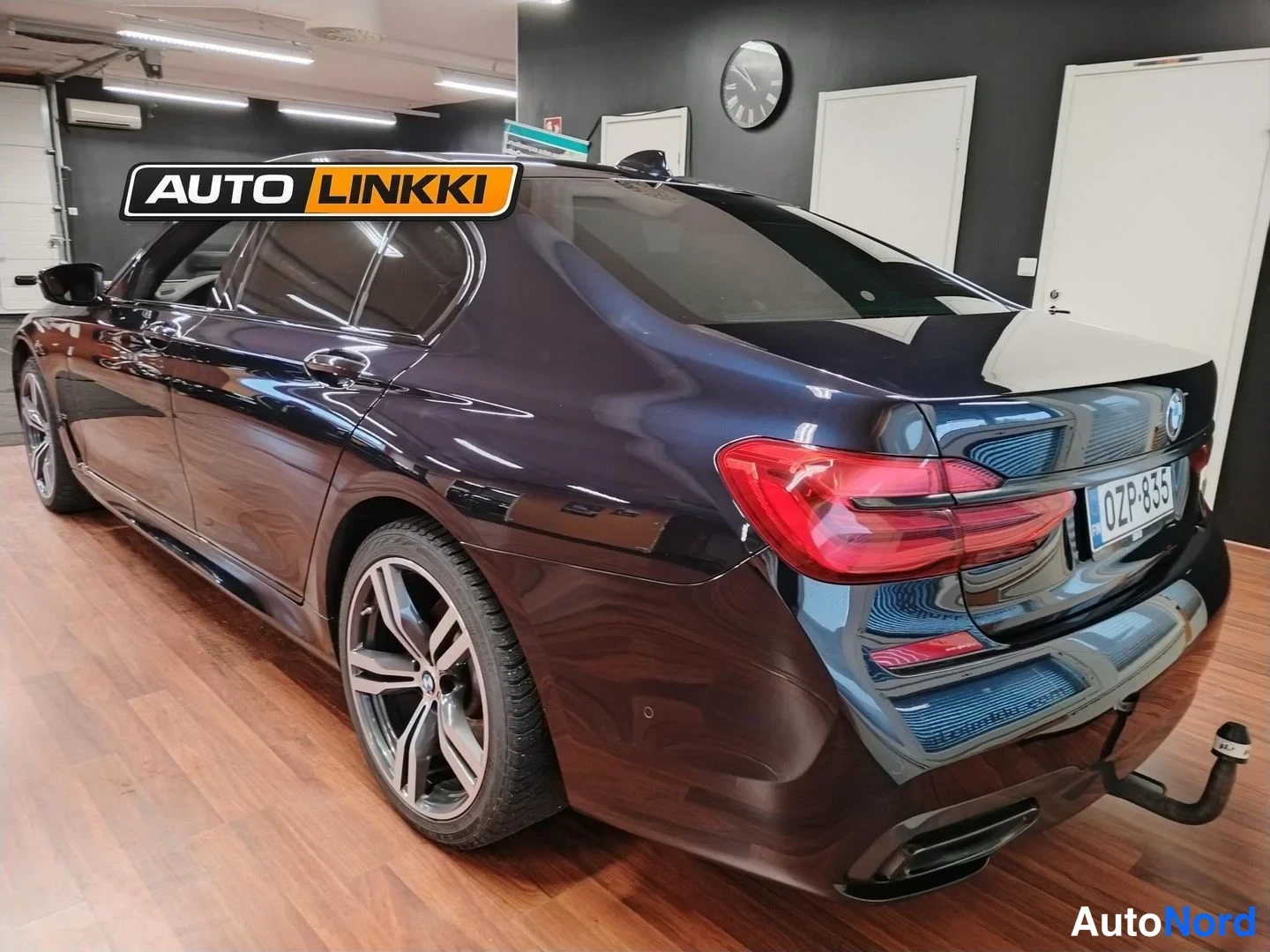 Takaviisto: Tummansinisen BMW-sedanin takakulma, rekisterikilpi ja luukkuasennossa oleva taaksekytketty vetokoukku näkyvissä.