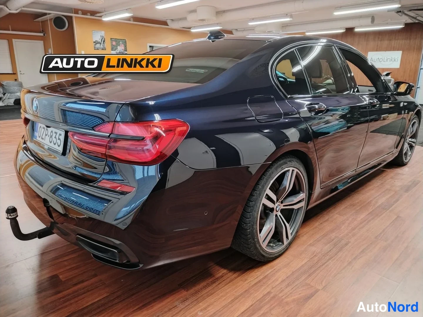 Takaviisto: Tummansinisen BMW-sedanin takakulma toiselta sivulta, rekisterikilpi ja vetokoukku luukussa näkyvissä.