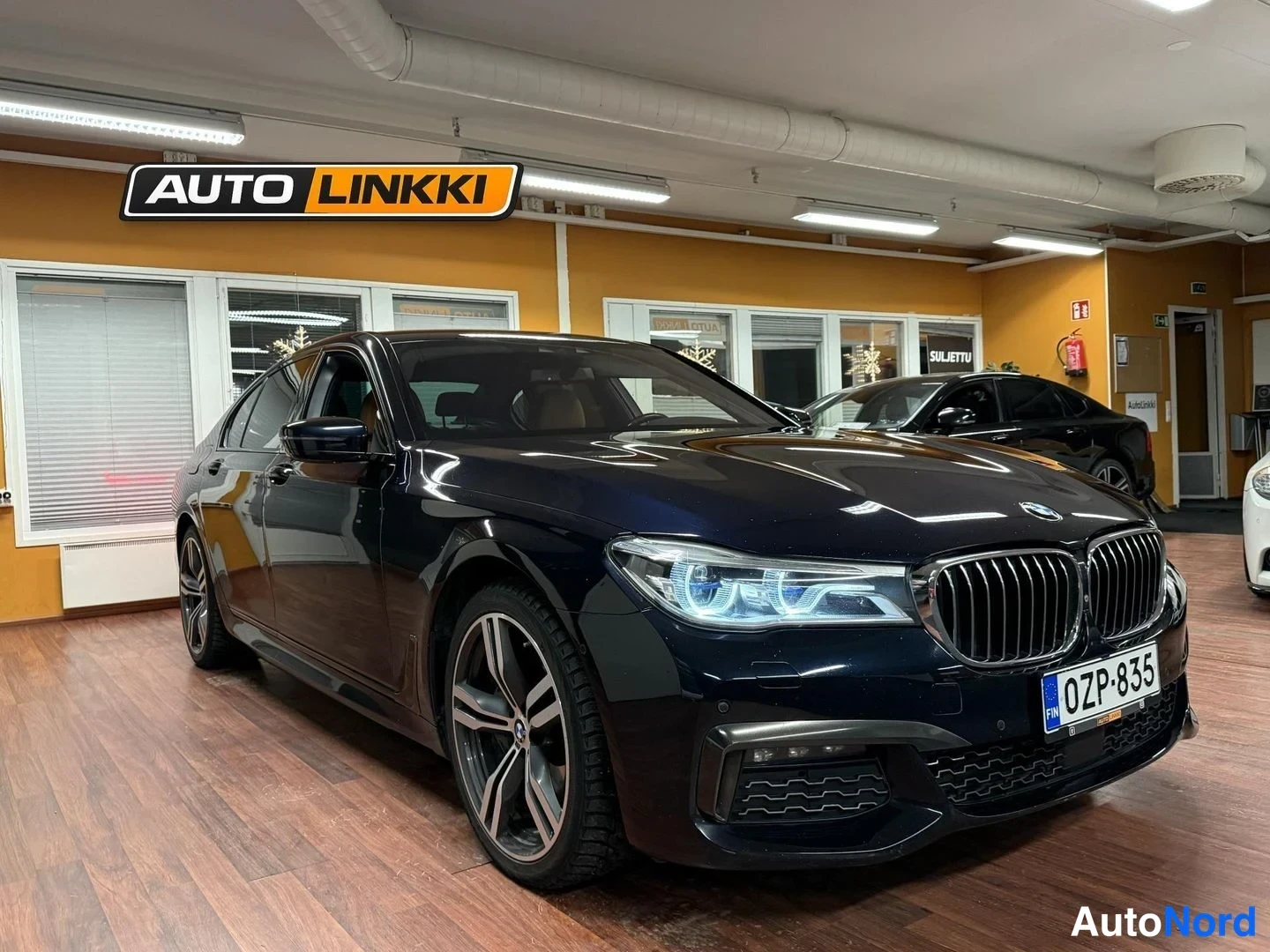 Etuviisto, nokka oikealle: Mustan sininen BMW-henkilöauto etu-kulmanäytössä sisätiloissa, tunnuskilpi.