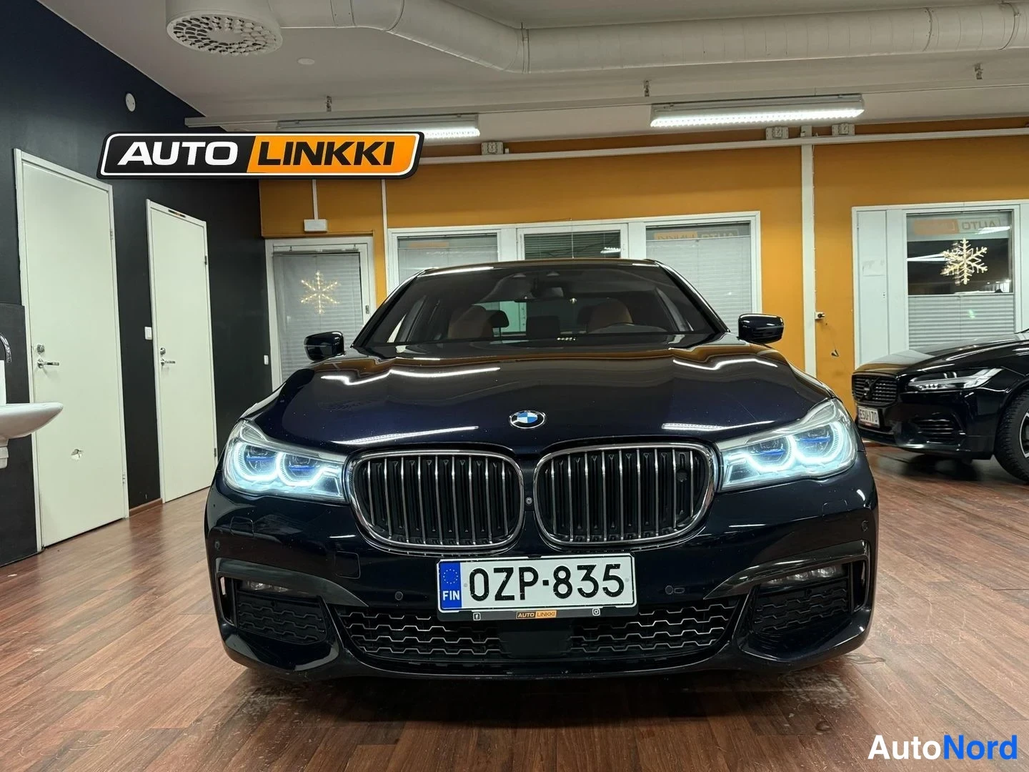 Edestä: Tumman sinisen BMW-henkilöauton etupää etualassa sisätiloissa, tunnuskilpi.