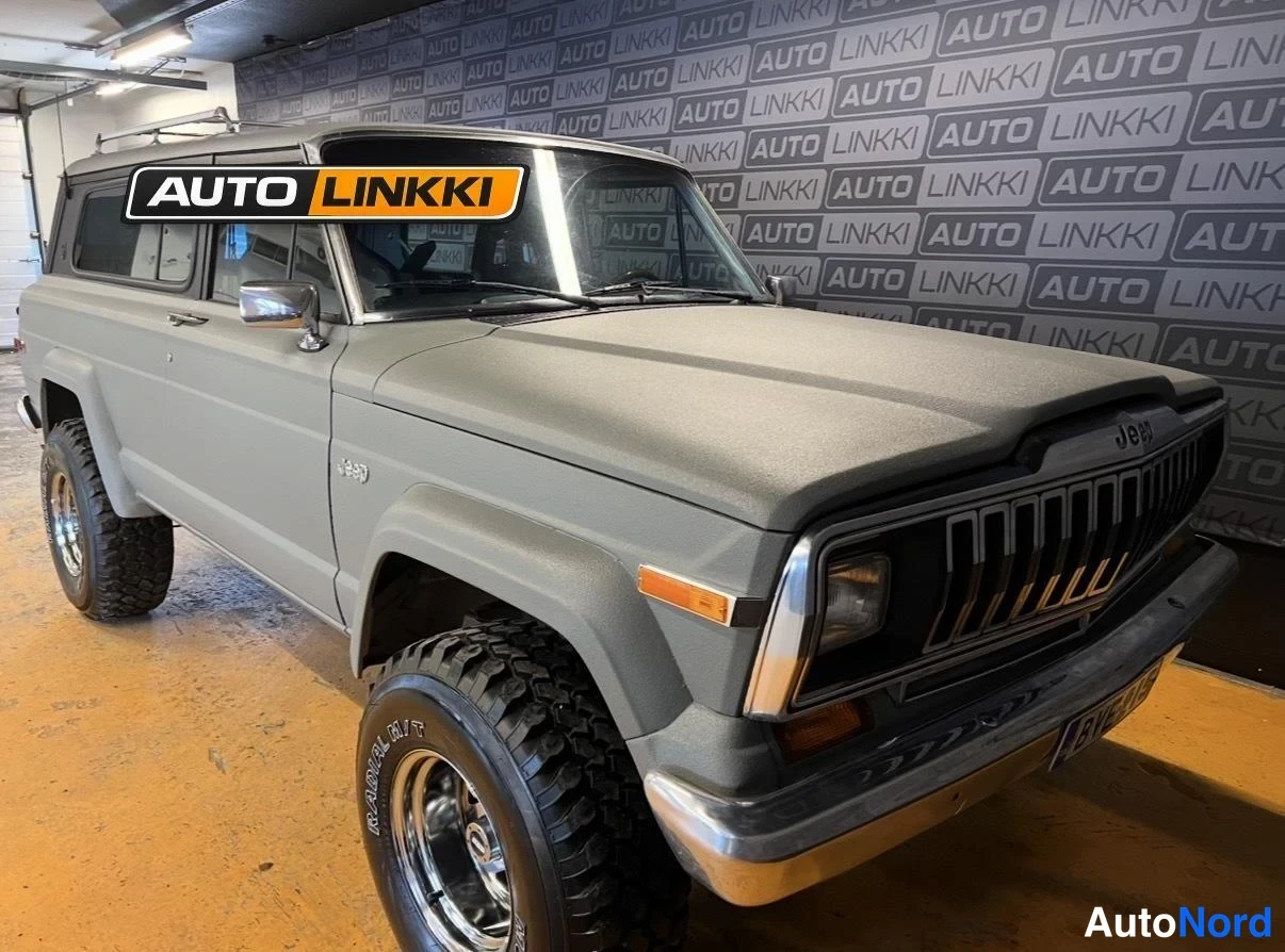 Etuviisto, nokka oikealle: Harmaa Jeep Cherokee mustalla Jeep-tekstillä varustetulla etusäleiköllä, kuva oikeasta etukulmasta.