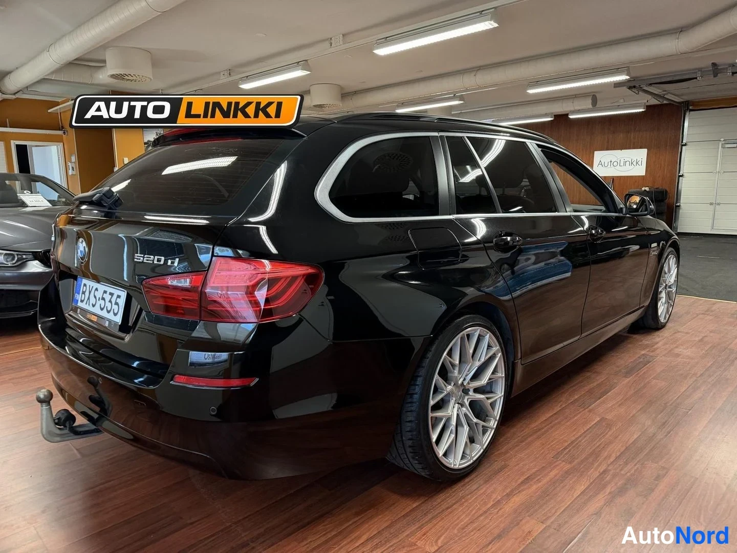 Takaviisto: Musta BMW 520d Touring takaviisto sisätiloissa, rekisteritunnus, lukkiutumattomat sumuvalot ja vetokoukku näkyvissä.