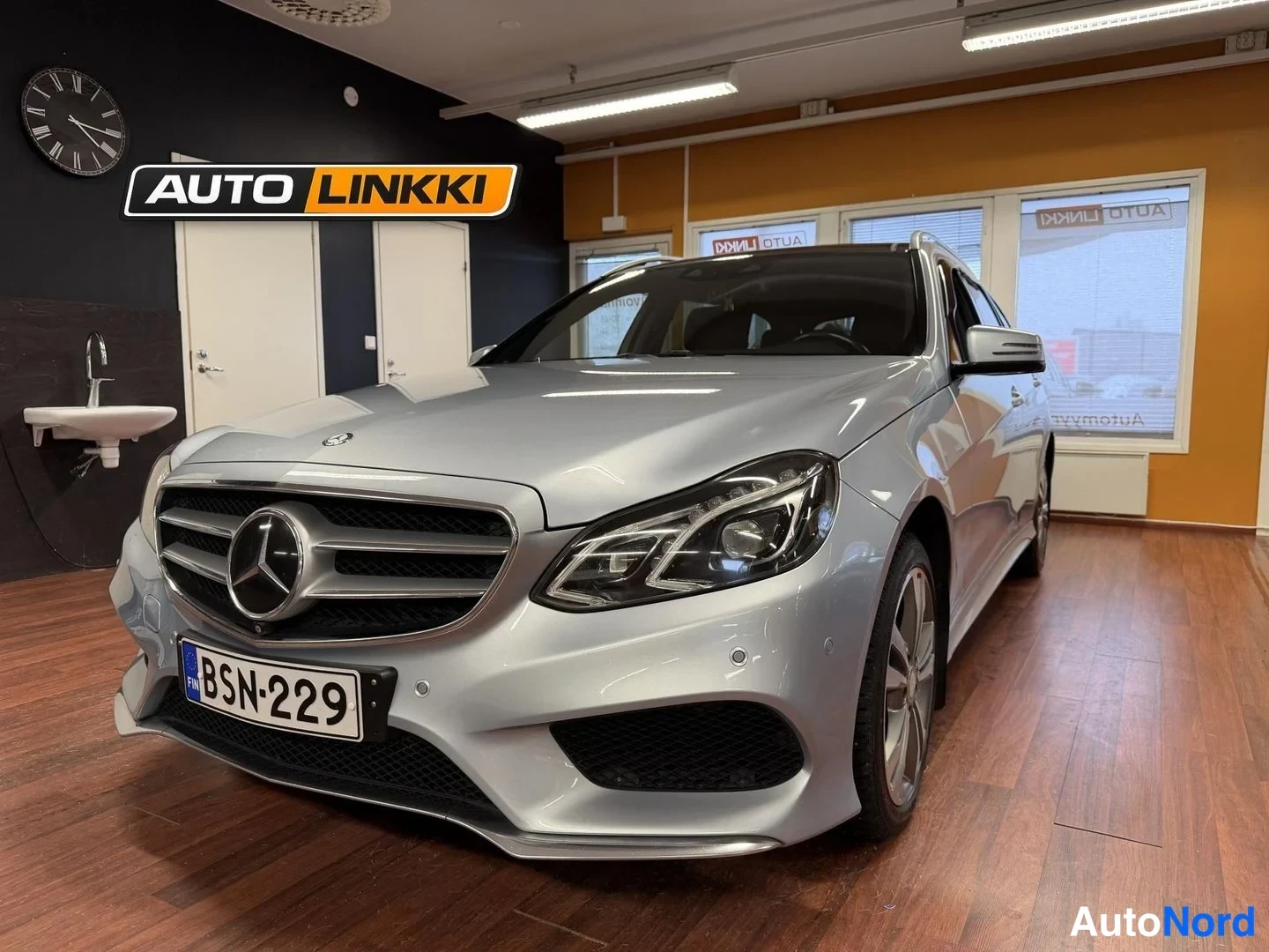 Etuviisto, nokka vasemmalle: Hopeanvärinen Mercedes-Benz etu kolmannesvasen kulma showroomissa, rekisterikilpi.