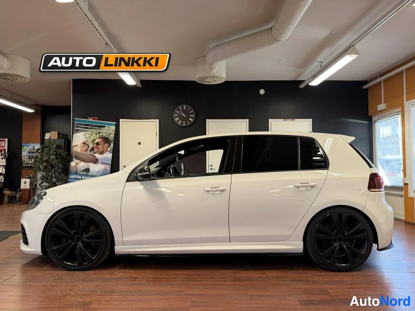 Sivulta: Valkoinen Volkswagen Golf sivukulmasta sisätiloissa, mustat vanteet ja tummat takaluukut.