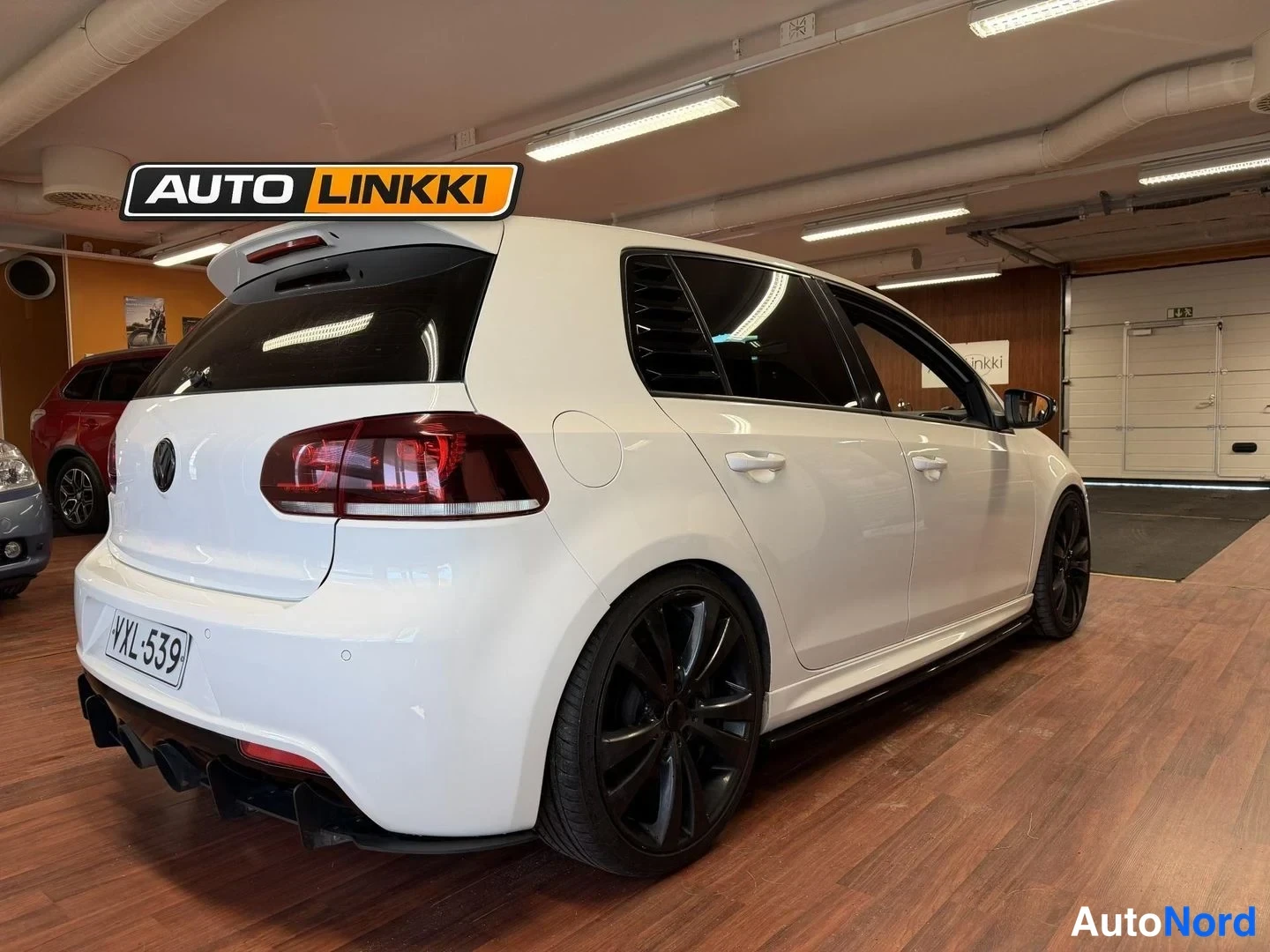 Takaviisto: Valkoinen Volkswagen Golf takakulmasta toiselta sivulta, tummat takavalot, mustat vanteet ja neljä pakoputkea, rekisteri.