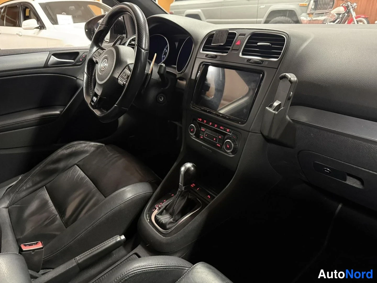 Muu: Auton ohjaamo vasemmalta: Volkswagen-ohjauspyörä, automaattivaihdevipu, kosketusnäyttö ja mustat penkit.