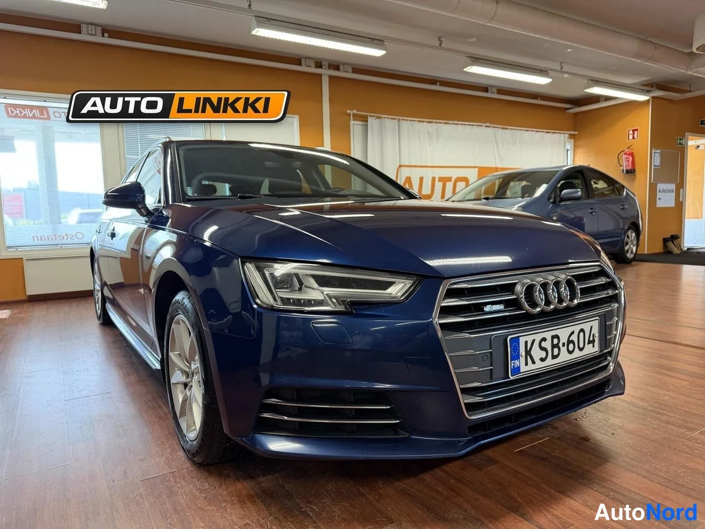 Etuviisto, nokka oikealle: Sininen Audi A4 Avant esitellään myymälässä, etunosa ja vasen kylki näkyvissä.