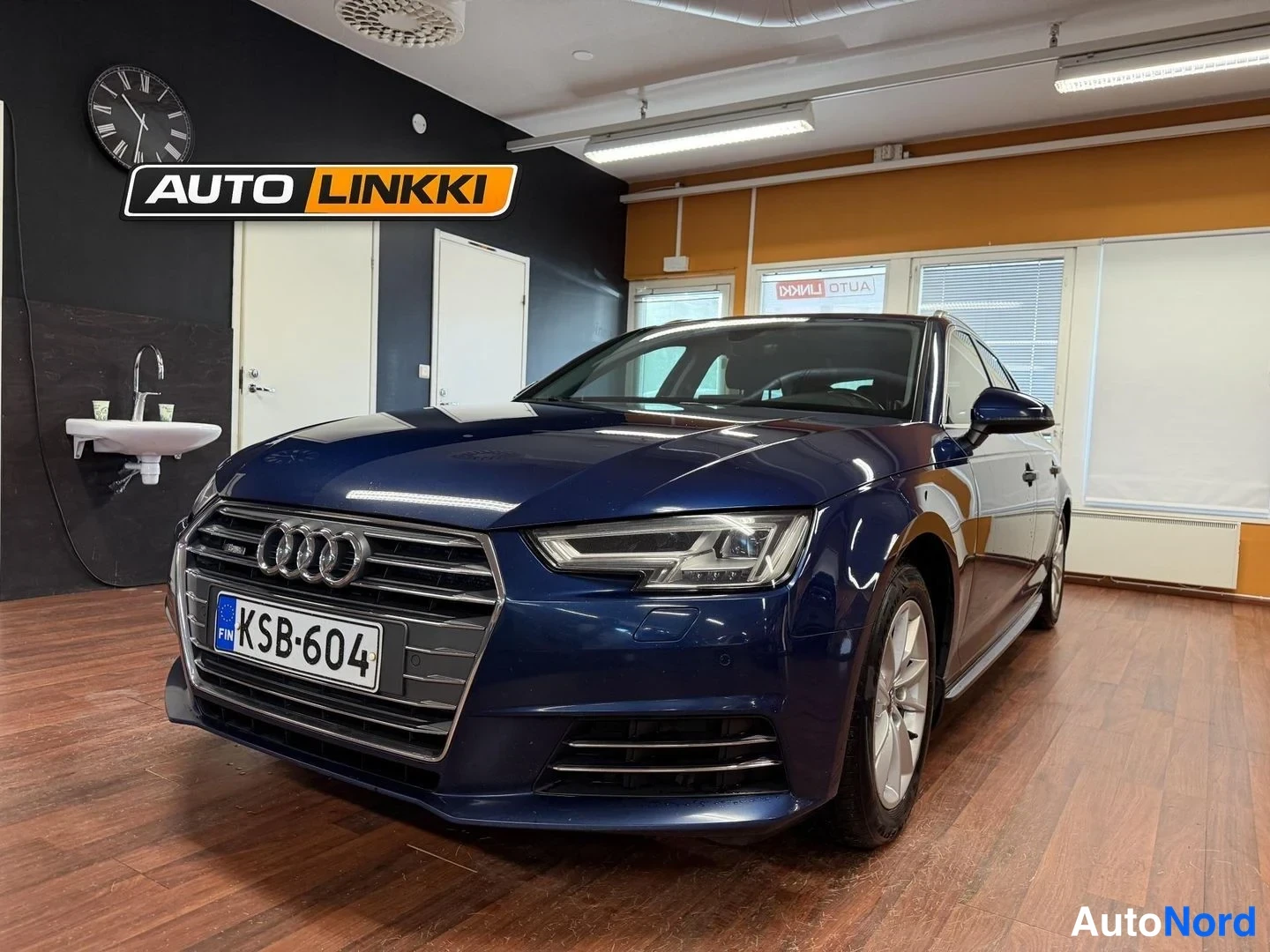Etuviisto, nokka vasemmalle: Tummansininen Audi A4 Avant myymälässä, keulakulta ja oikea kylki näkyvissä.
