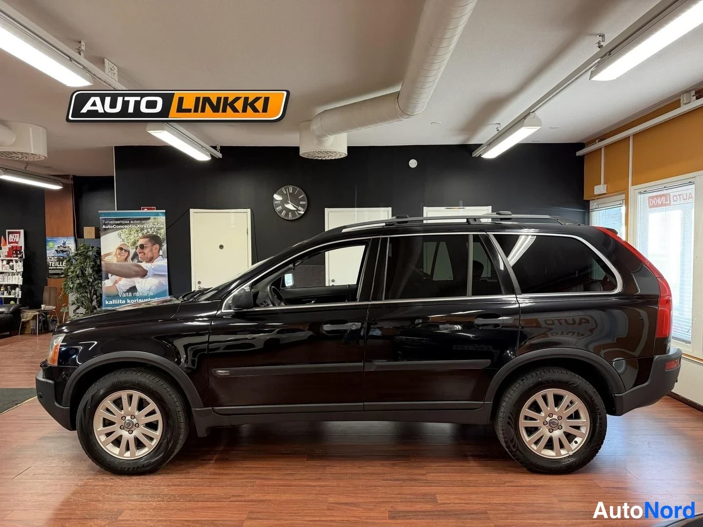 Sivulta: Mustan Volvo XC90 -maastoco kyljensuuntainen kuva sisätiloissa, kattokaiteet ja vaijerit näkyvissä.